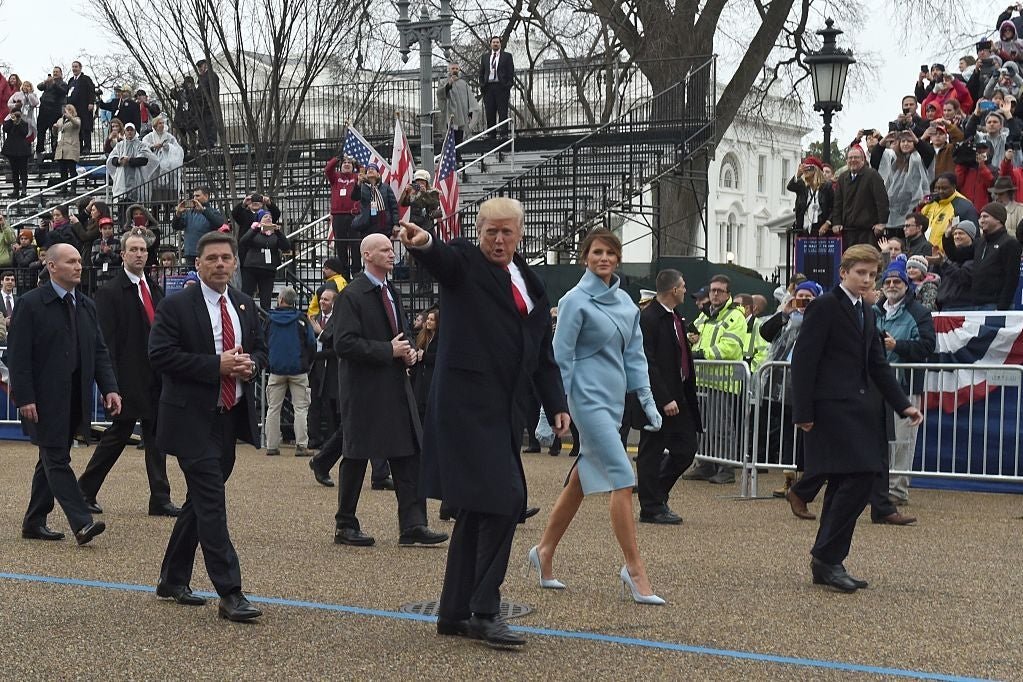 Donald Trump, who is pointing, Melania Trump, Barron Trump, and security officials walk past a mostly empty set of bleachers during the inaugural parade.