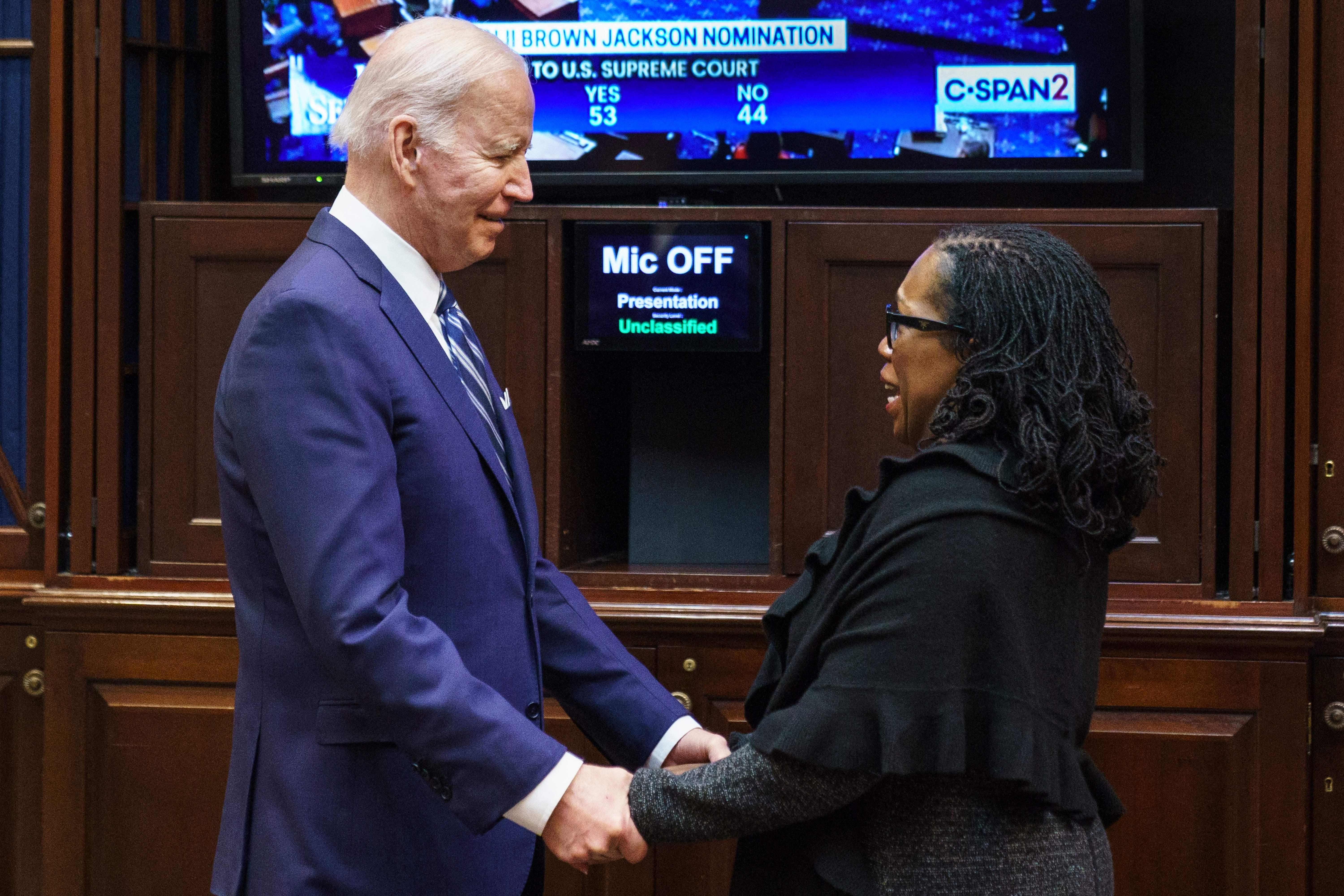Biden and Jackson clasp hands in front of a screen showing the Senate floor and the vote