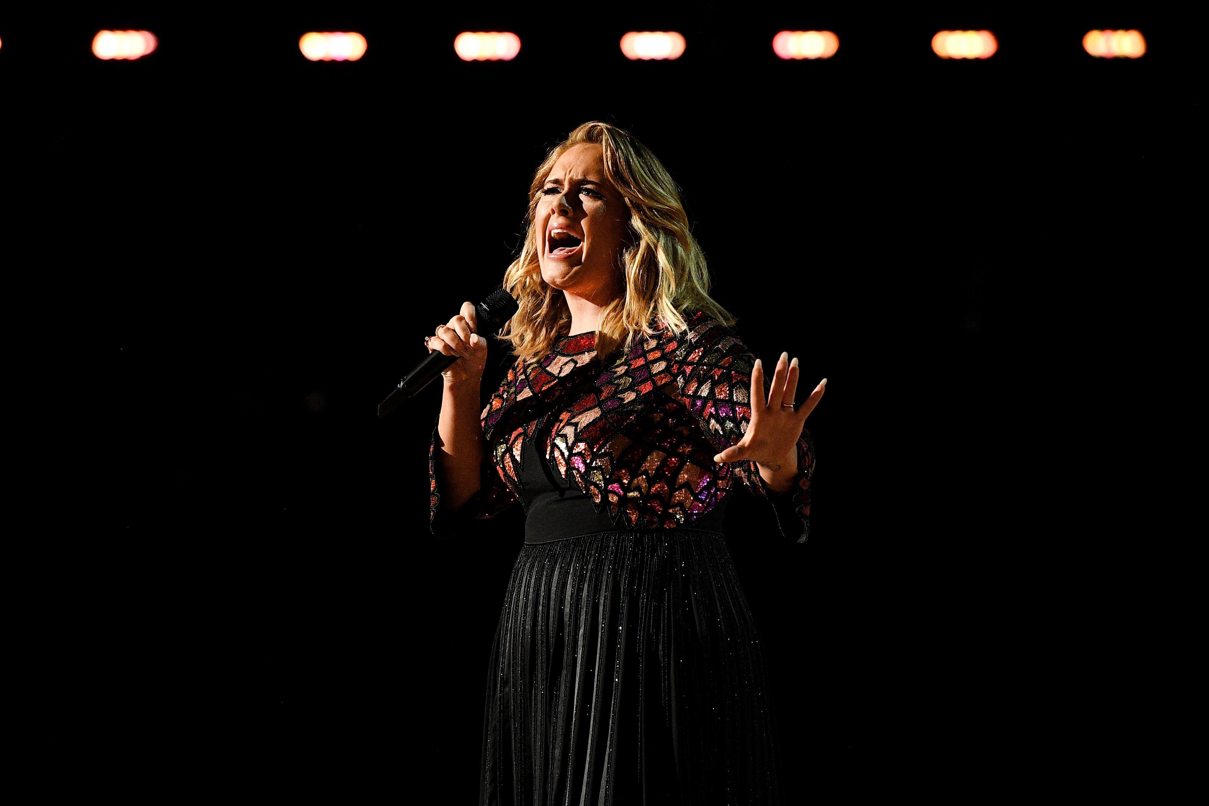 Adele sings into a microphone against a black backdrop.