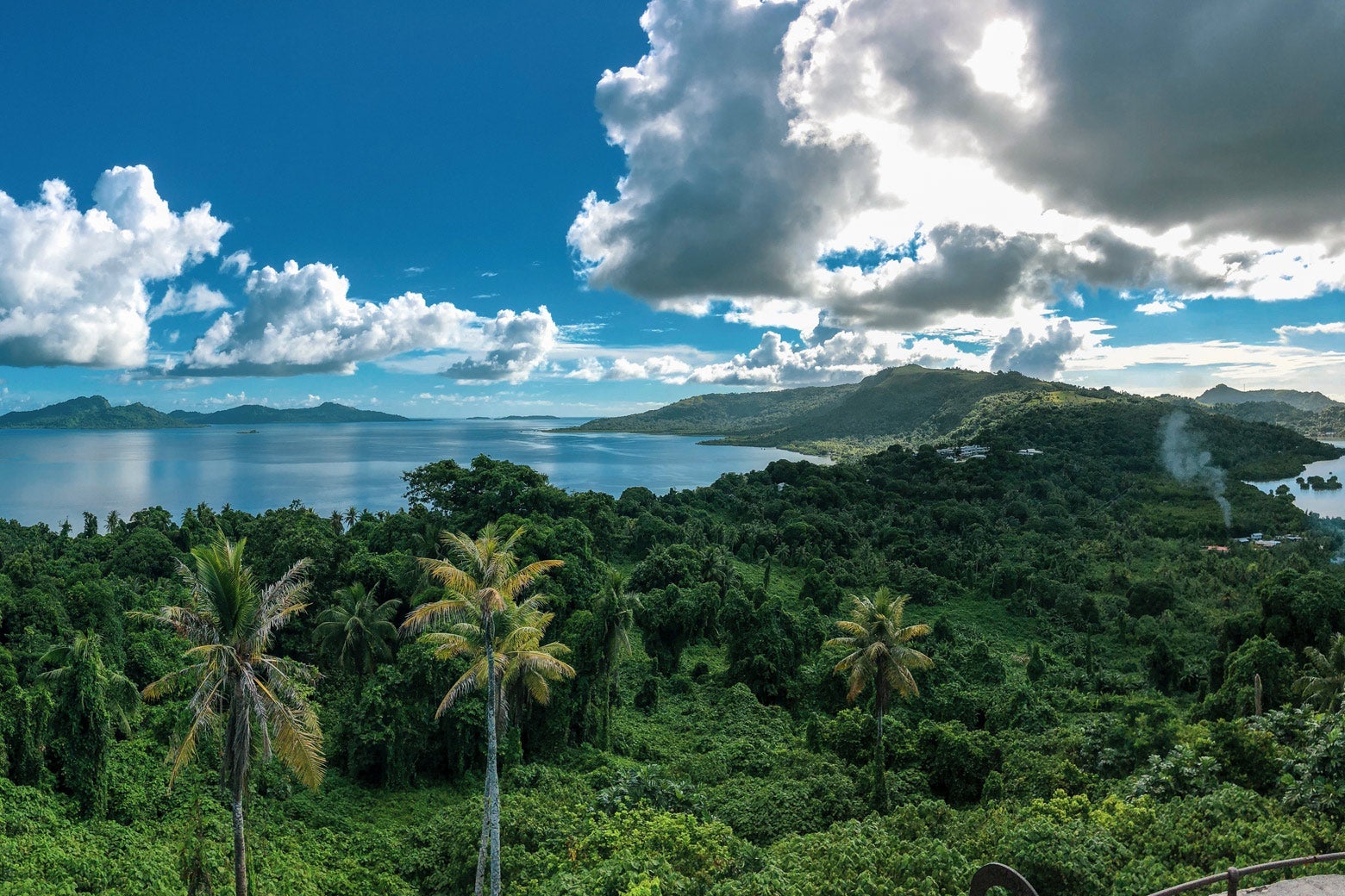 A landscape of lush forest, a lagoon, and a blue sky with white clouds.