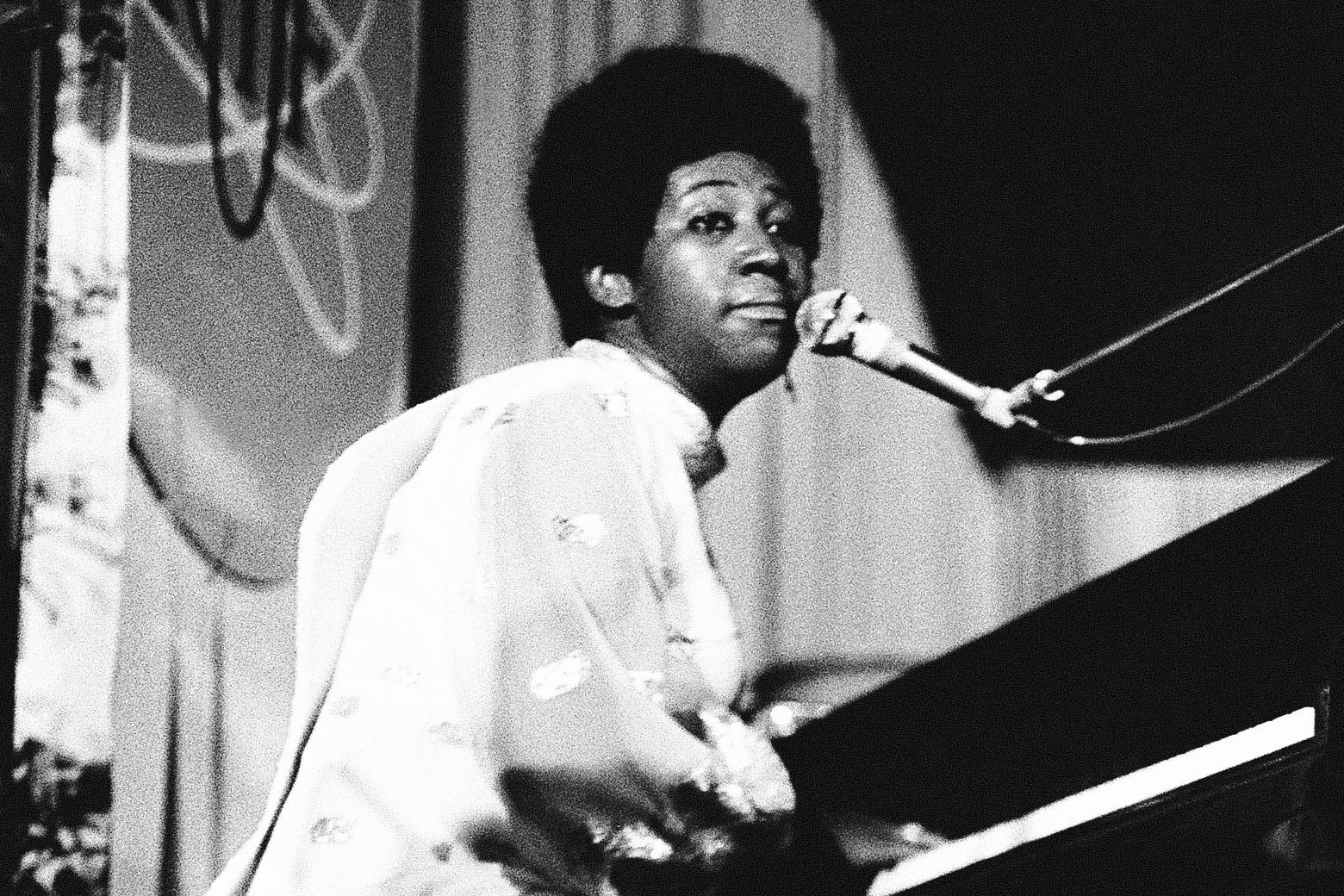 A black-and-white photo of Aretha Franklin at a piano.