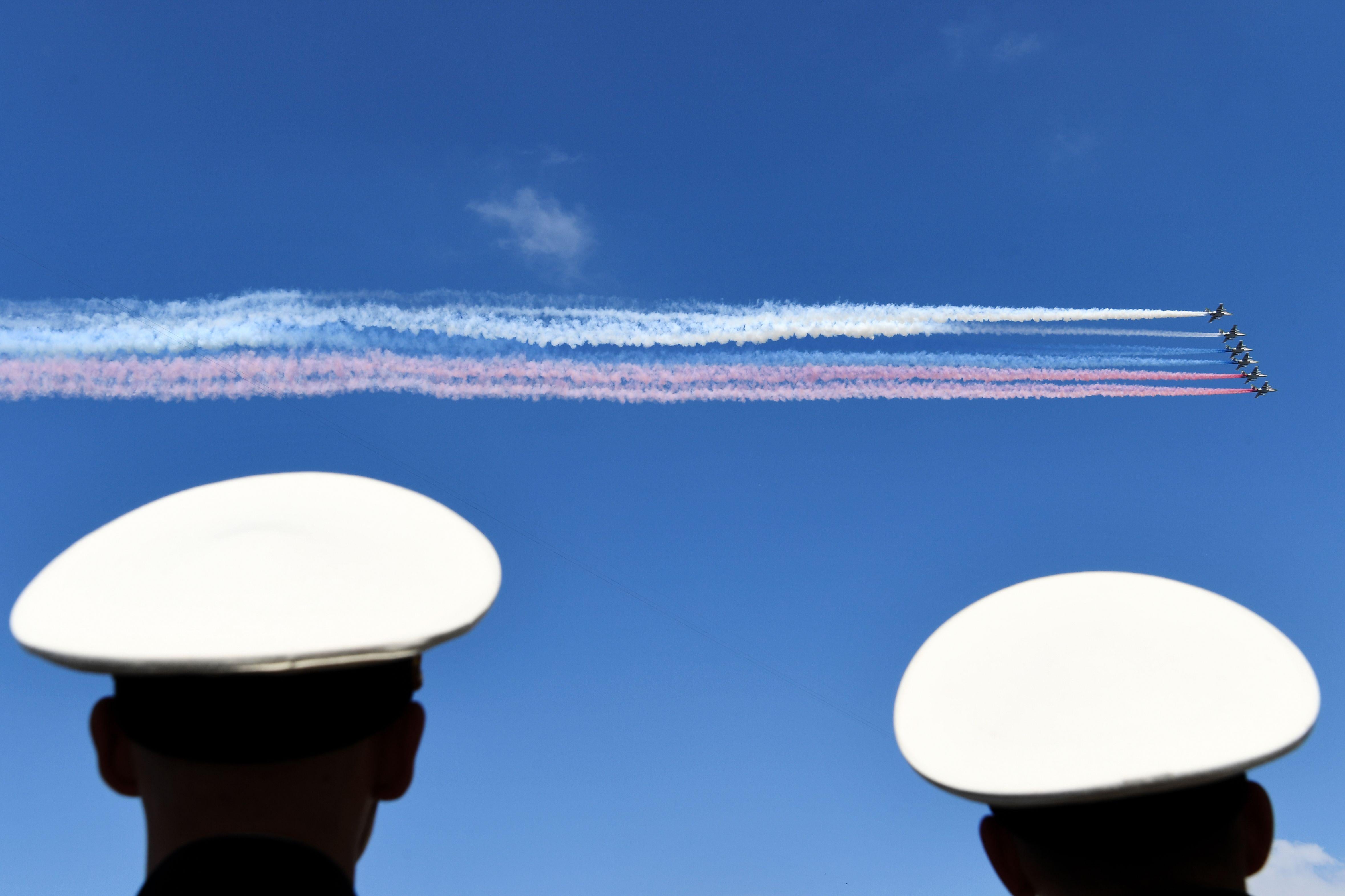 Russian aircraft release smoke in white, blue, and red, the colors of the Russian flag, while flying above the Neva River during the Navy Day parade in Saint Petersburg on July 29, 2018.