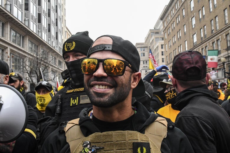 Enrique Tarrio wears sunglasses, a backward cap, and a bulletproof vest, during a downtown rally. 
