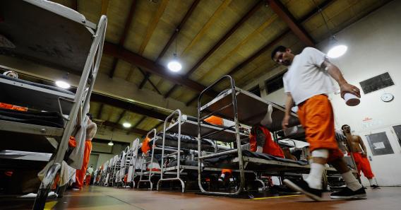 An inmate at Chino State Prison, which houses 5,500 inmates, walks past the double and triple bunk beds in a gymnasium that was modified to house 213 prisoners in Chino, Calif.