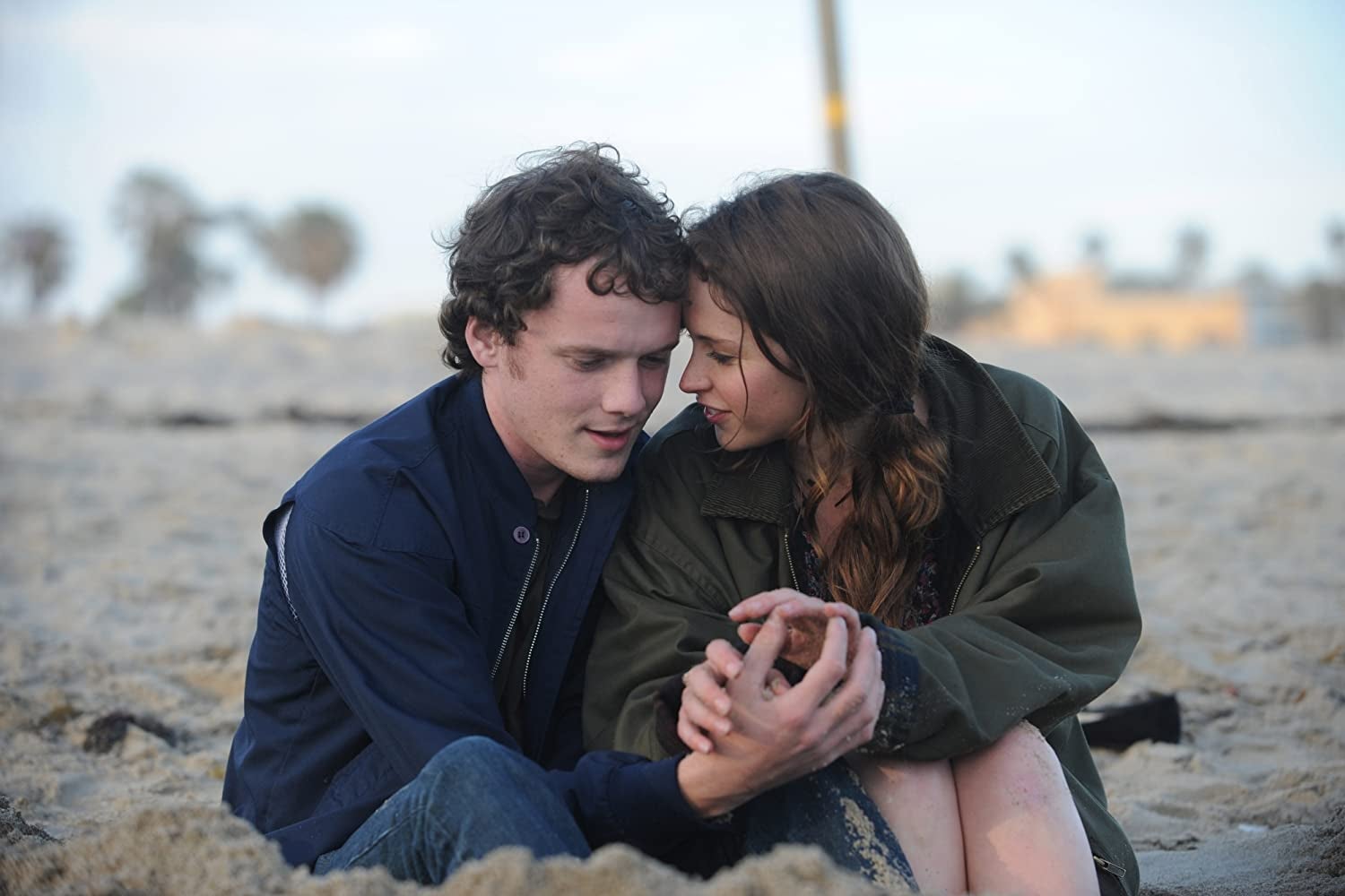 Anton Yelchin and Felicity Jones sit on a beach.