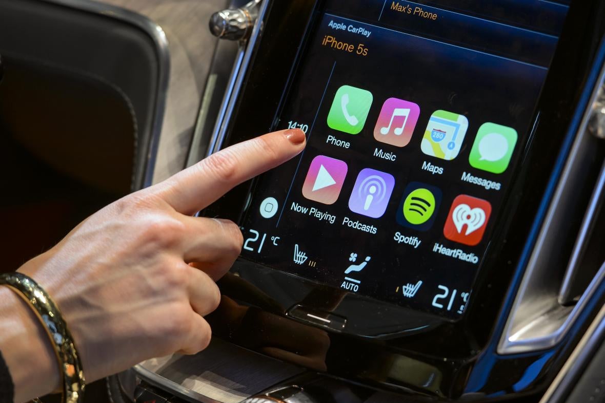 A finger reaches to touch an iPhone display on a screen inside a car.