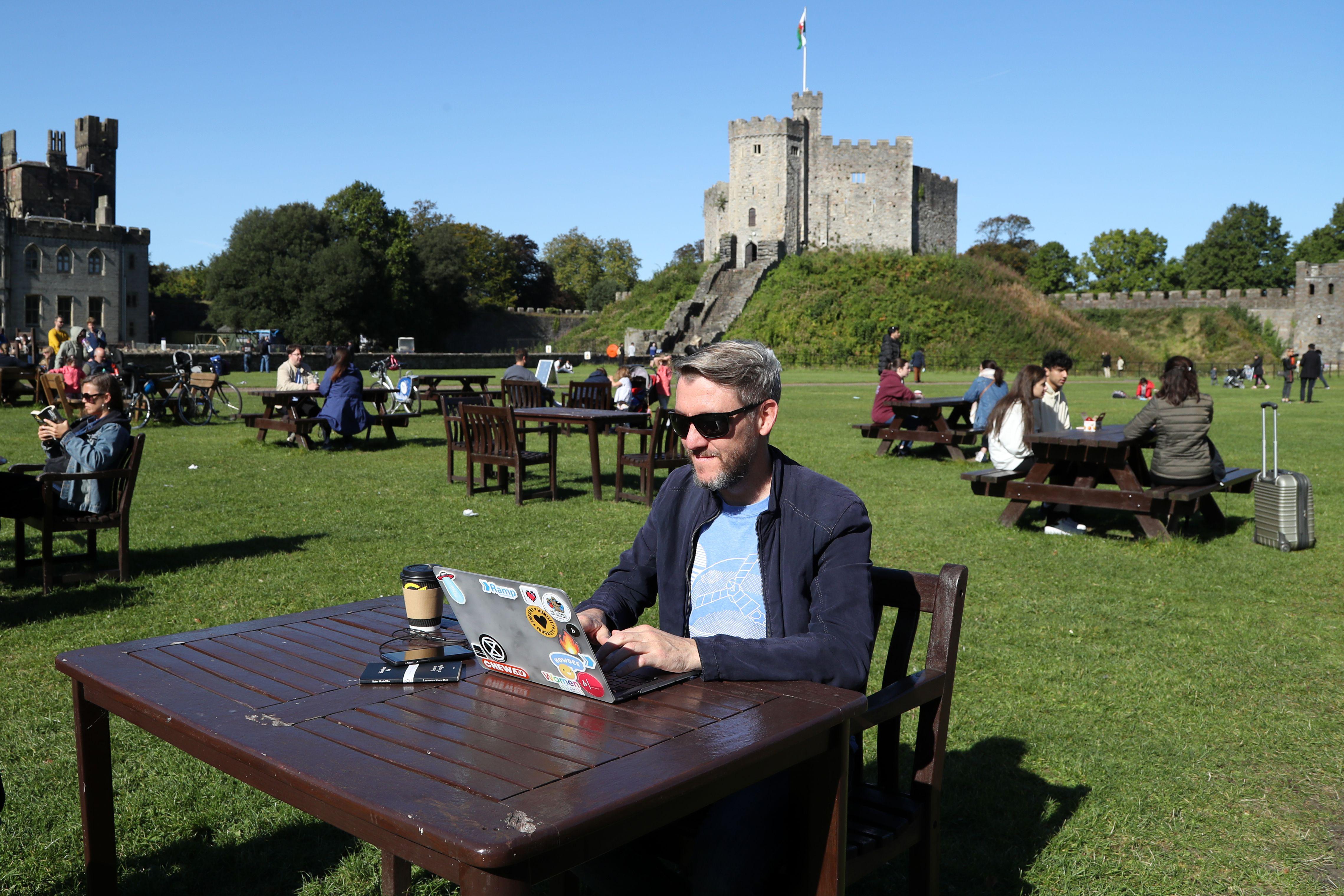 A man poses with his laptop computer in the late summer sunshine in the grounds of Cardiff Castle.