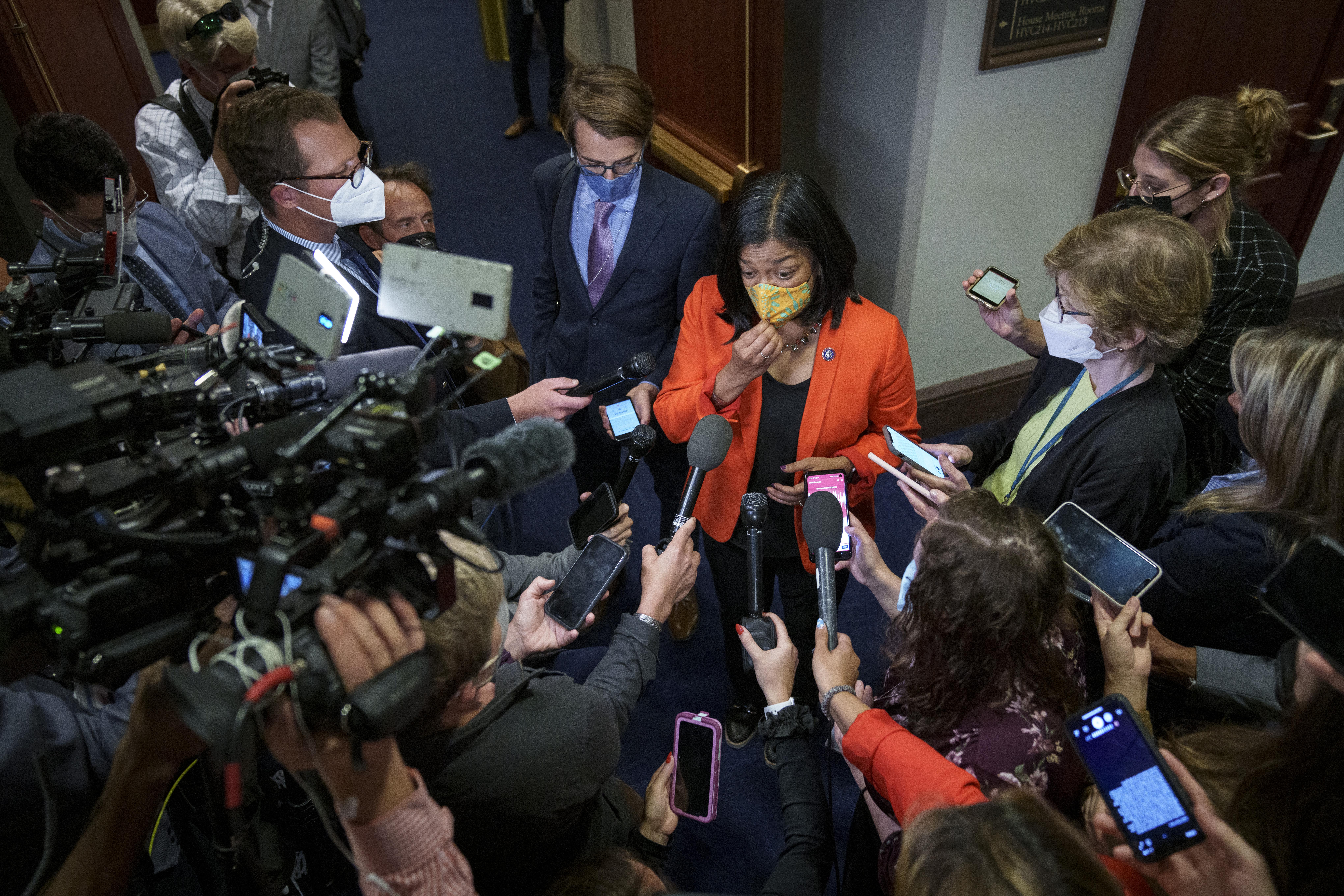 Jayapal standing in a hallway at the Capitol surrounded by reporters holding out phones and microphones for interviews