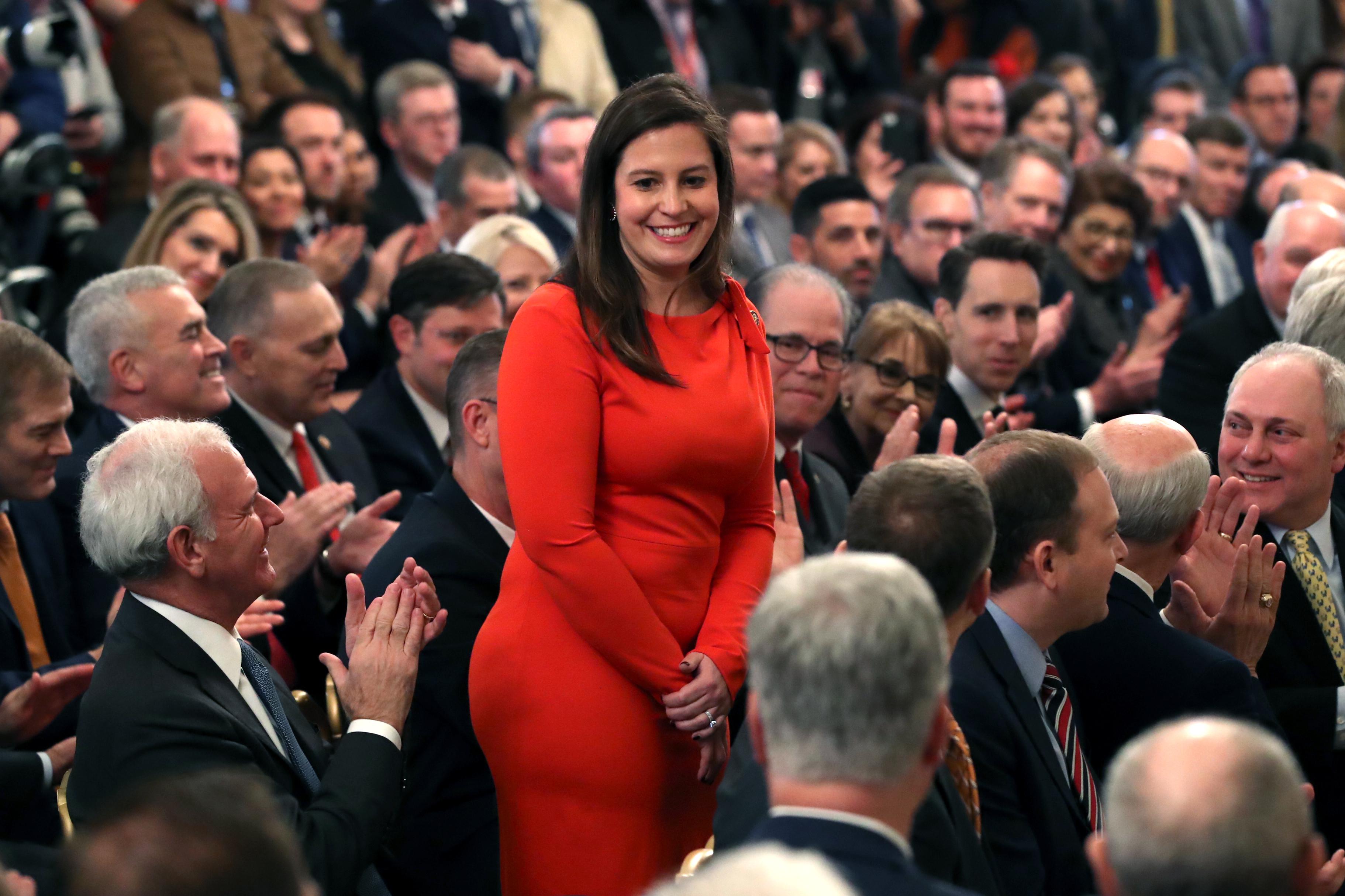 Stefanik stands and smiles as people seated close together around her applaud, some smiling at her
