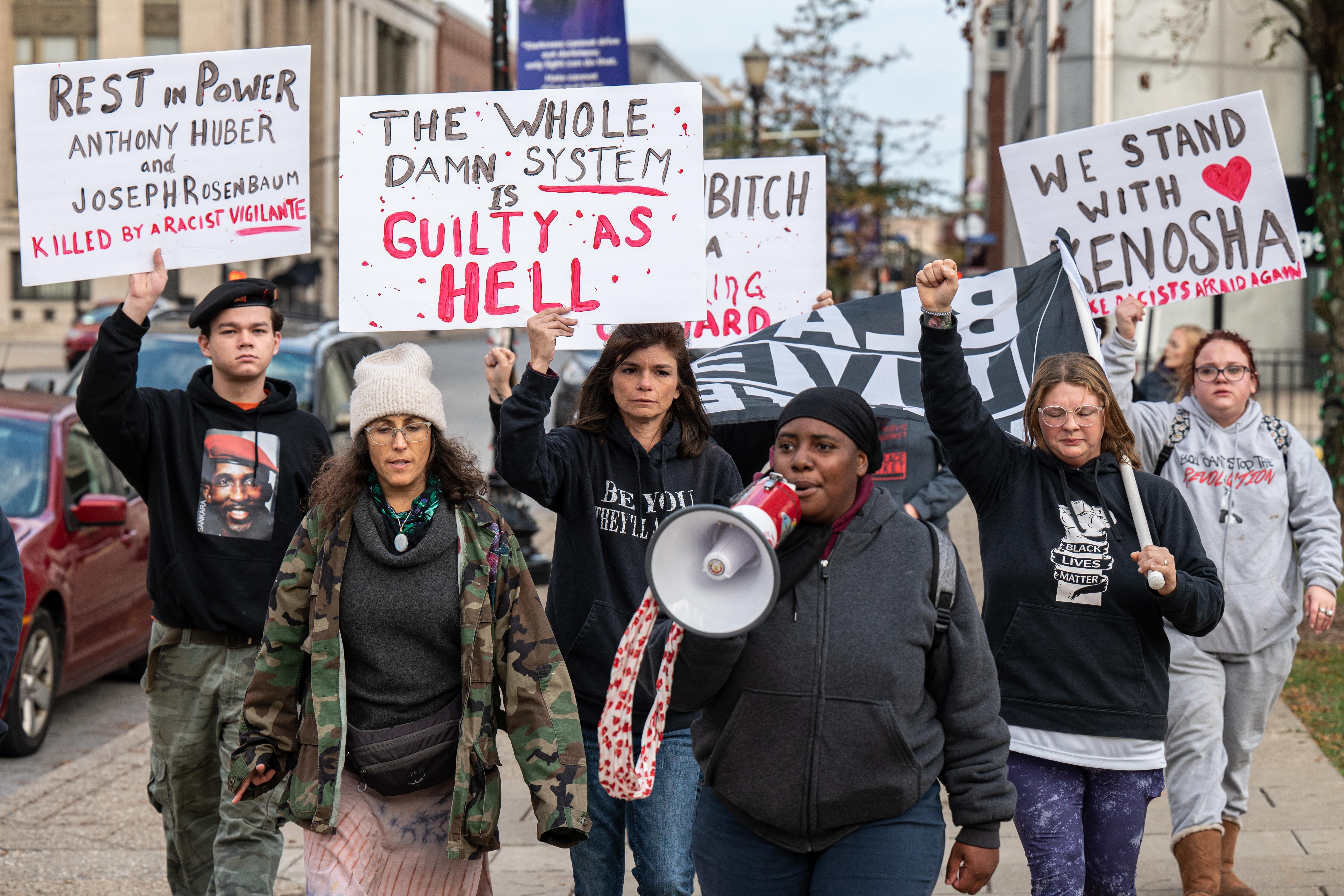 A group of people hold up signs. A Black woman at the front speaks into a megaphone.