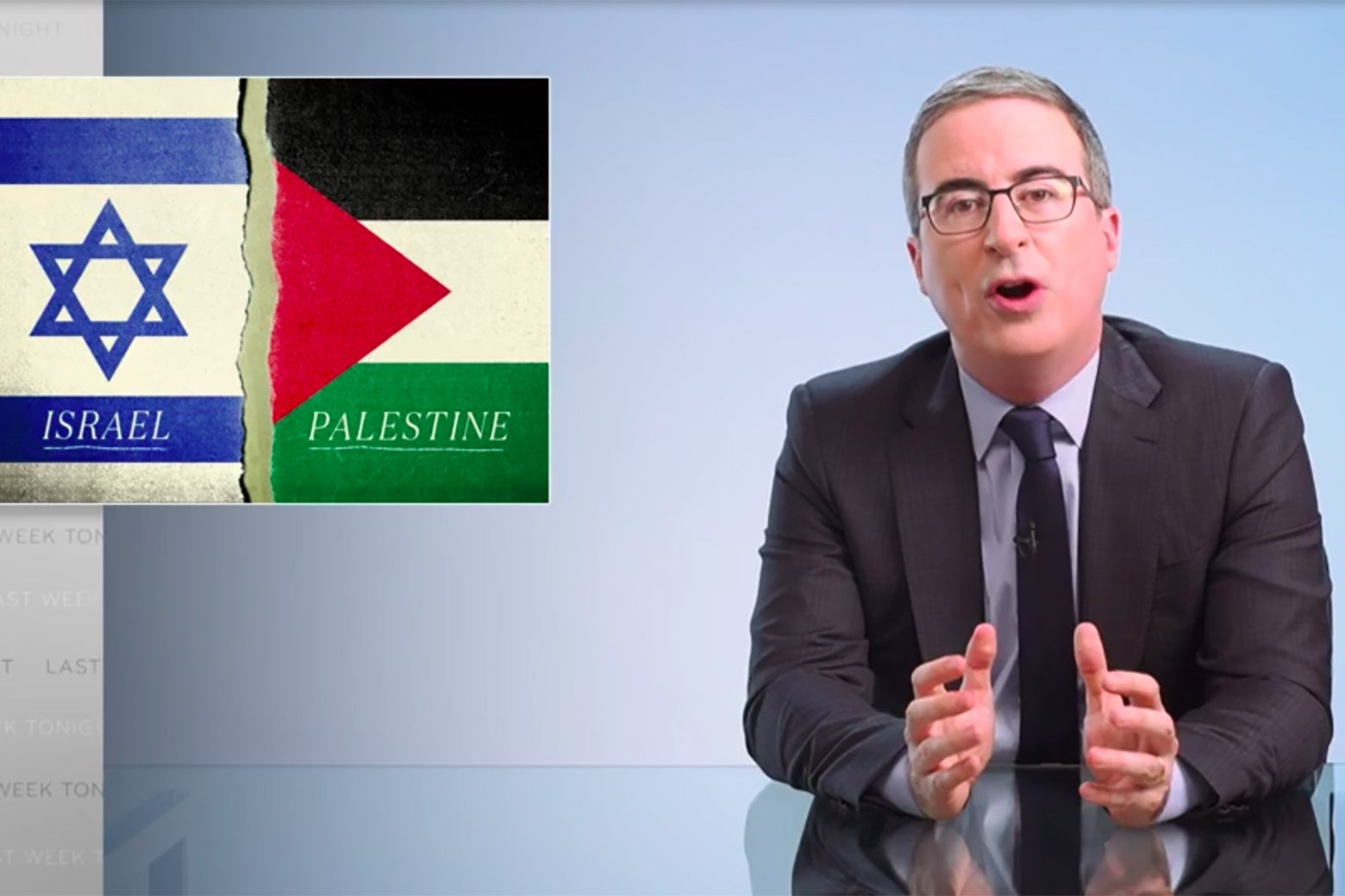 John Oliver sits at his glass anchorperson desk, in front of a graphic showing Israeli and Palestinian flags.