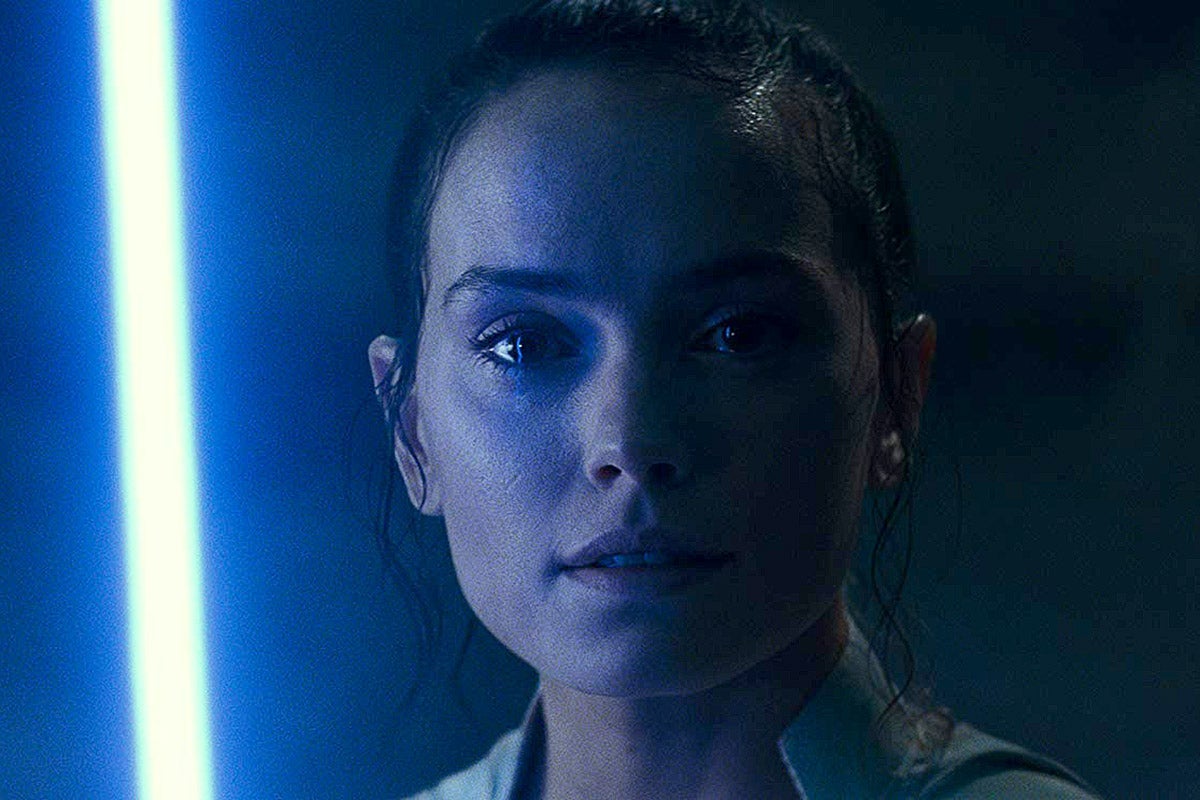 Daisy Ridley with a blue lightsaber to her left.