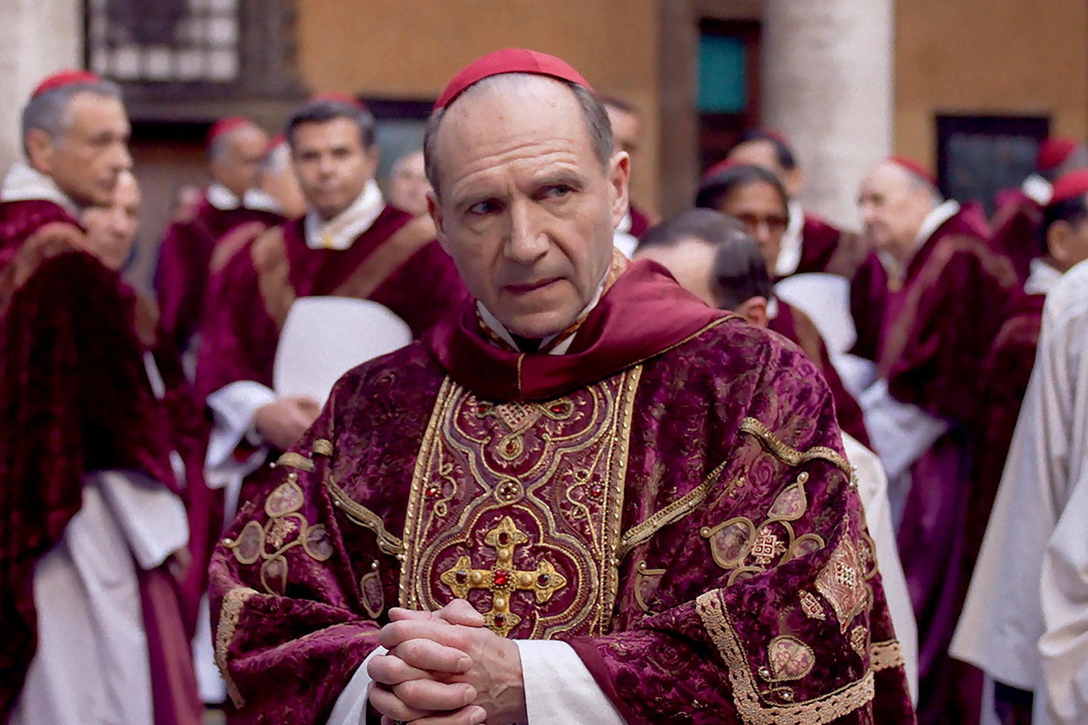 A cardinal in vestments, in a crowd of other cardinals, looks around suspiciously.