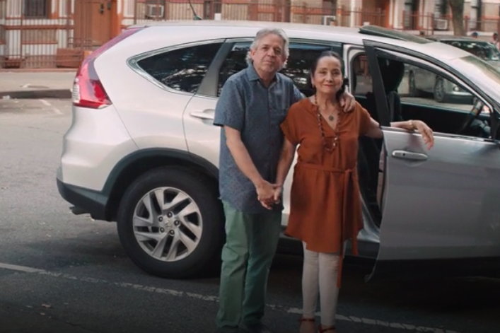 Standing in front of a silver car, Luis Miranda has his arm around Dr. Luz Towns-Miranda.