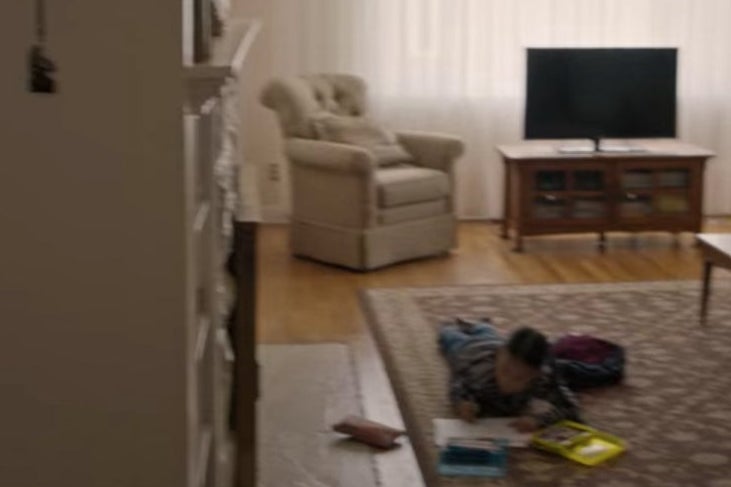 Ju Ju colors while laying on the rug in a living room and her grandfather sits in a chair.