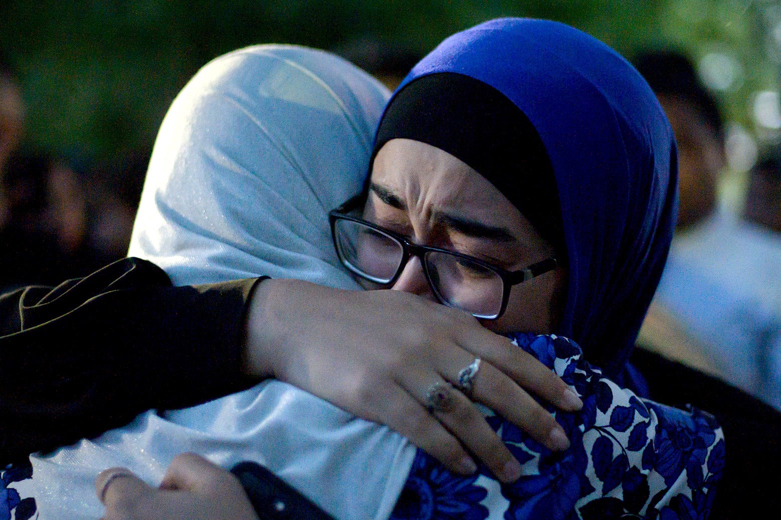 Two women wearing head scarves cry and hug.