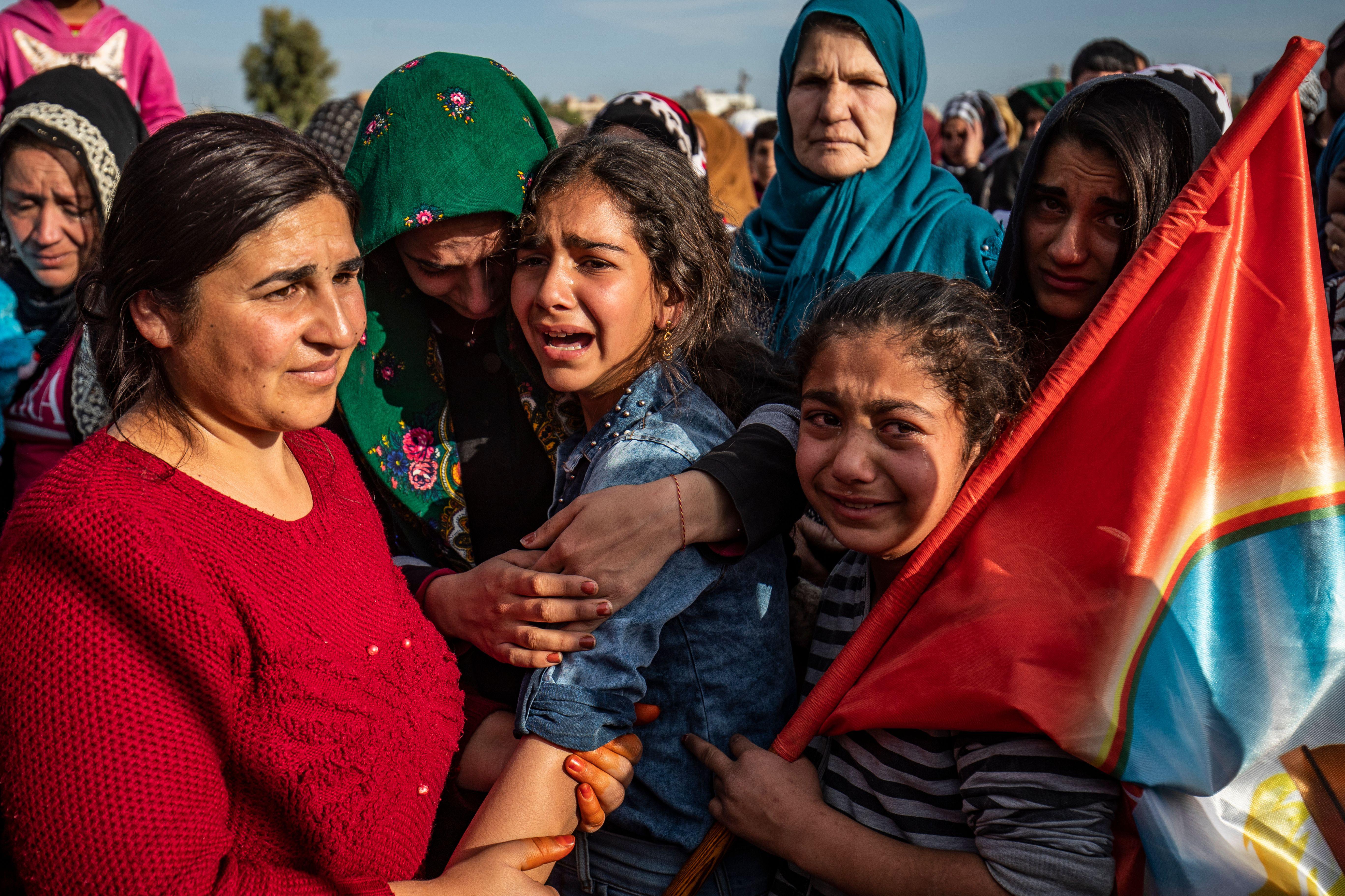 Women and children crying. One is holding a flag.