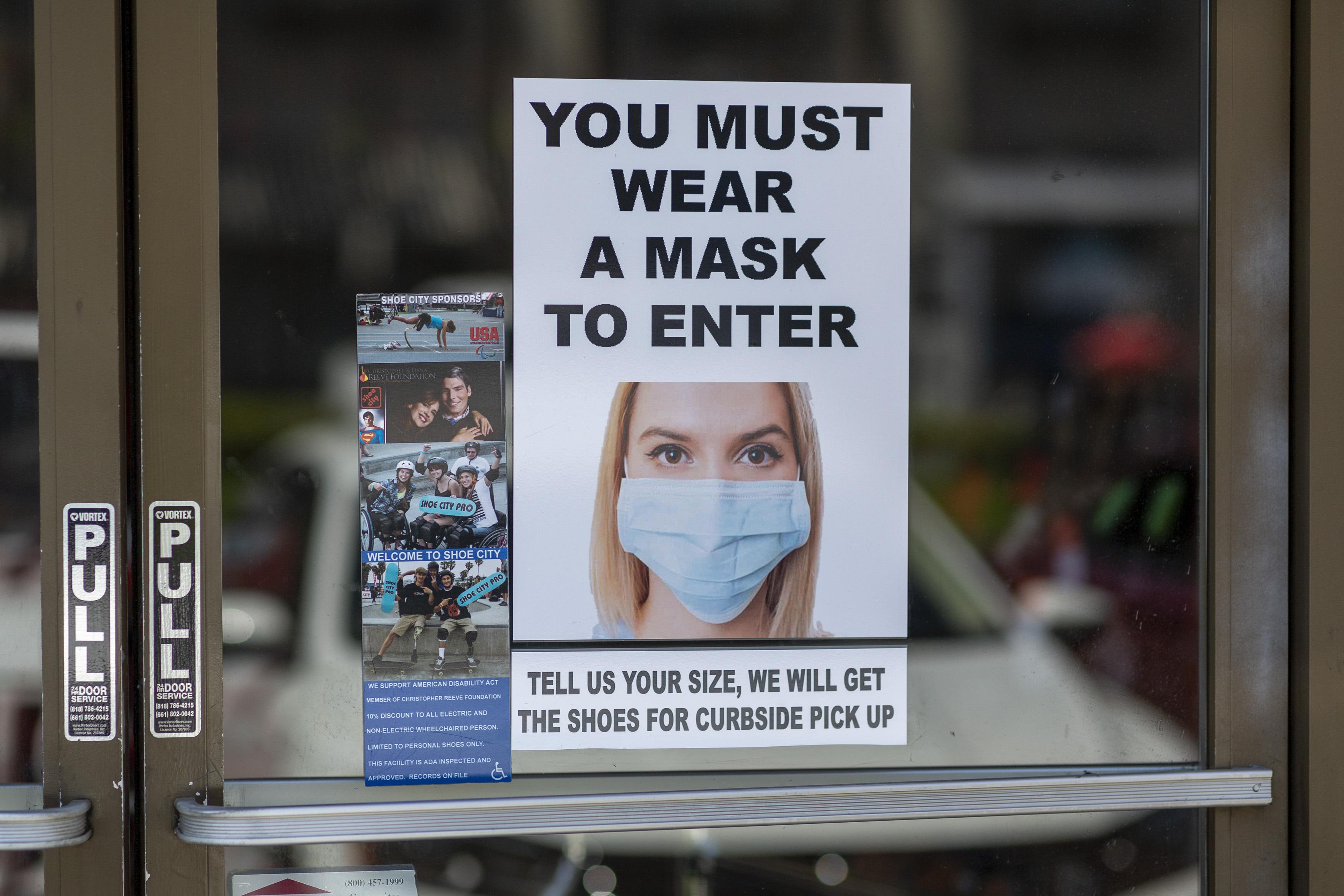 A sign on a glass door says "You must wear a mask to enter" and shows a photo of a woman wearing a face mask.