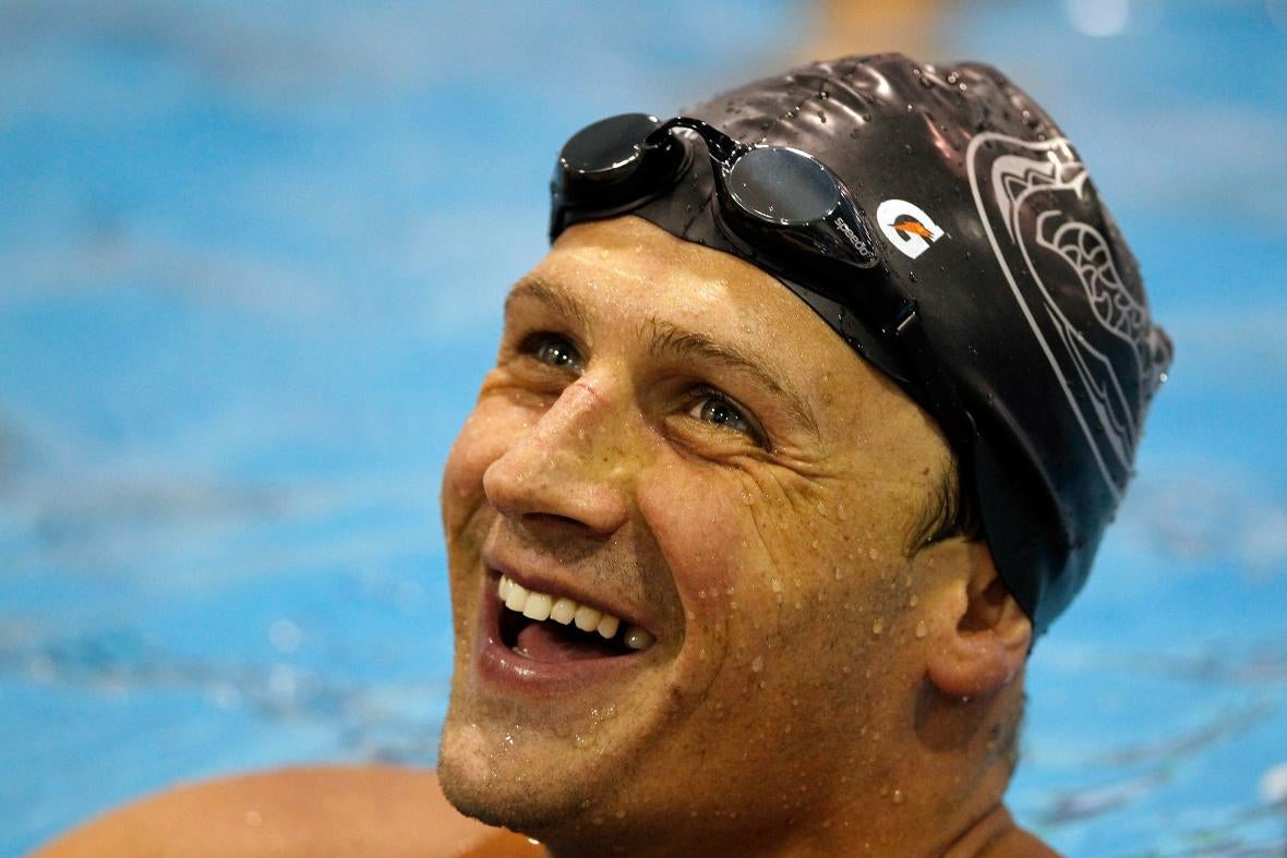 Lochte in swim cap and goggles on his forehead, looking up from the pool and smiling