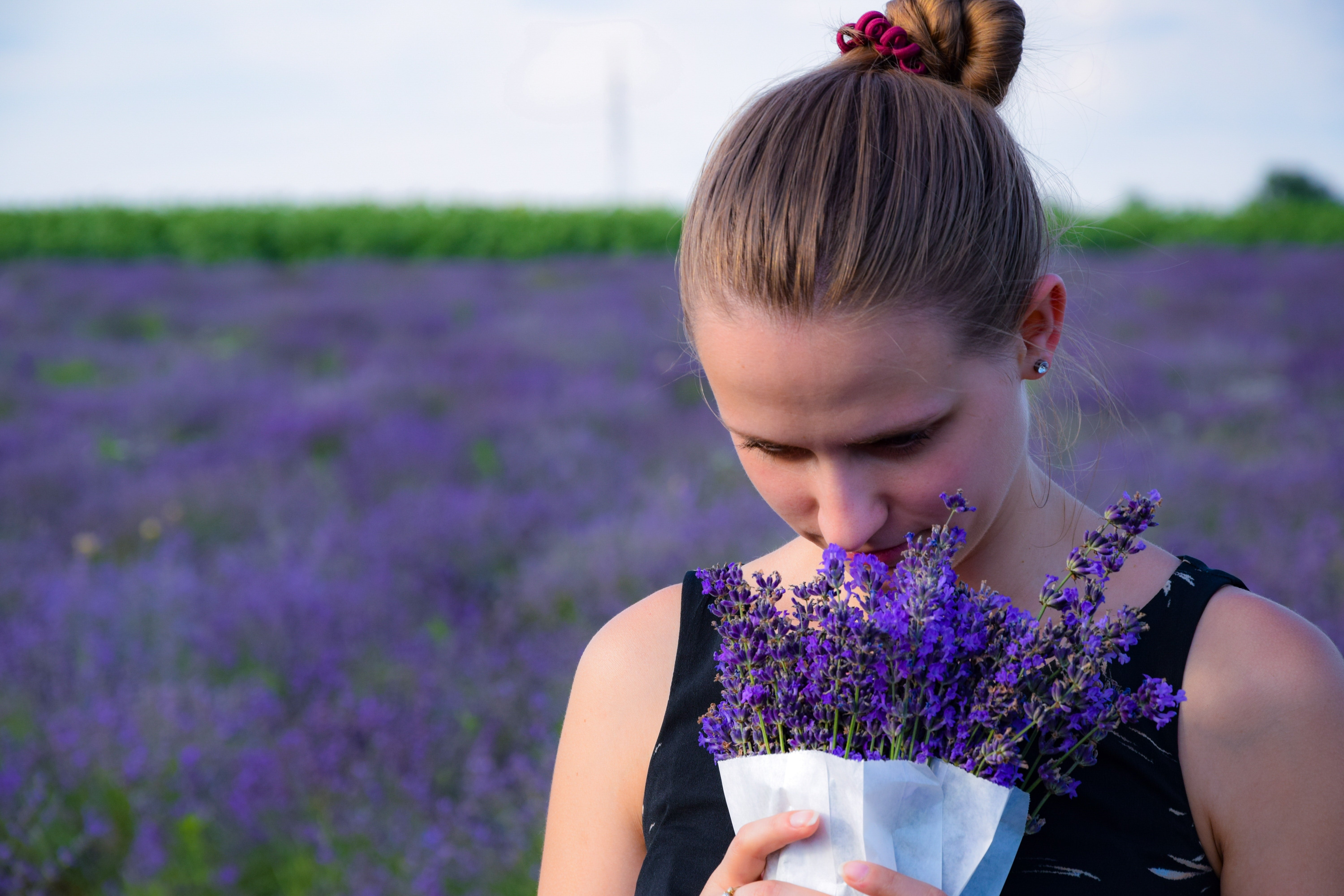 A woman smelling a bunch of lavender. There is a field of lavender behind her. 