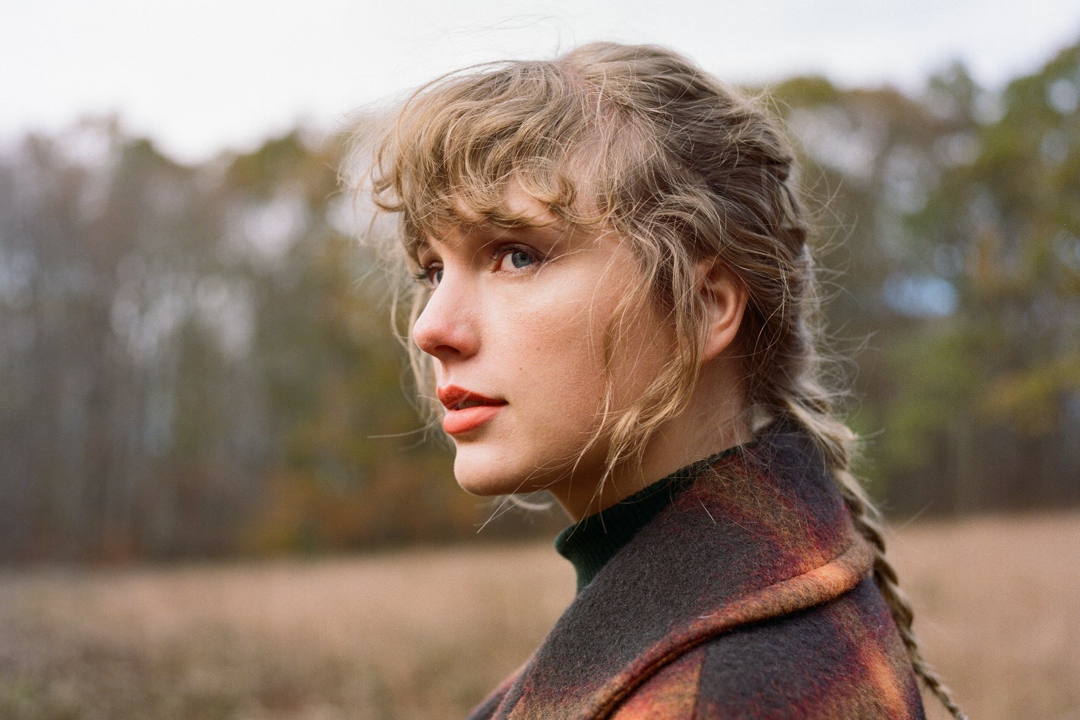 Taylor Swift, in a wintry field, in a braid and a plaid coat.
