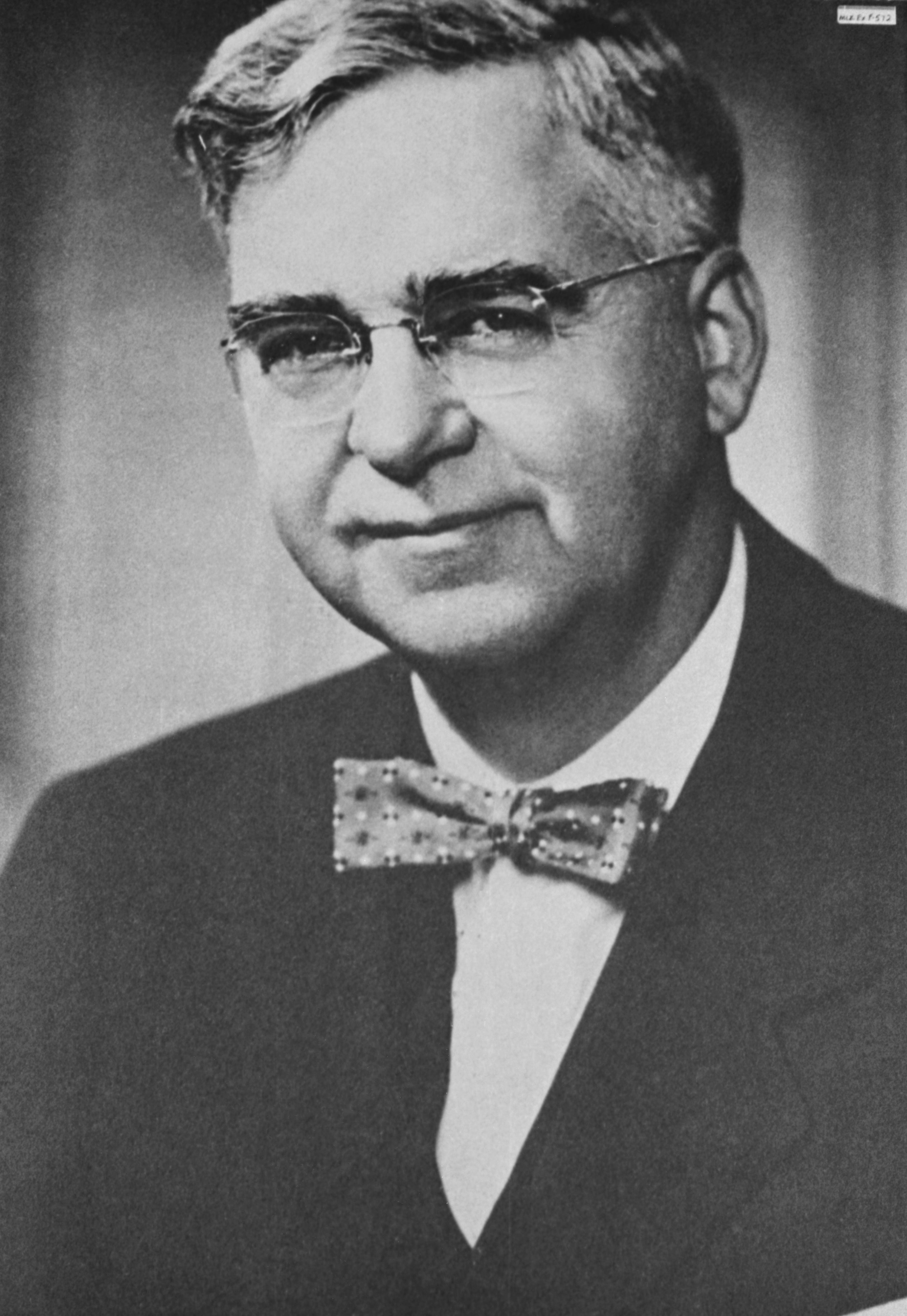 Black-and-white image of a white man with salt-and-pepper hair, wearing glasses, a black jacket, and a bow tie.