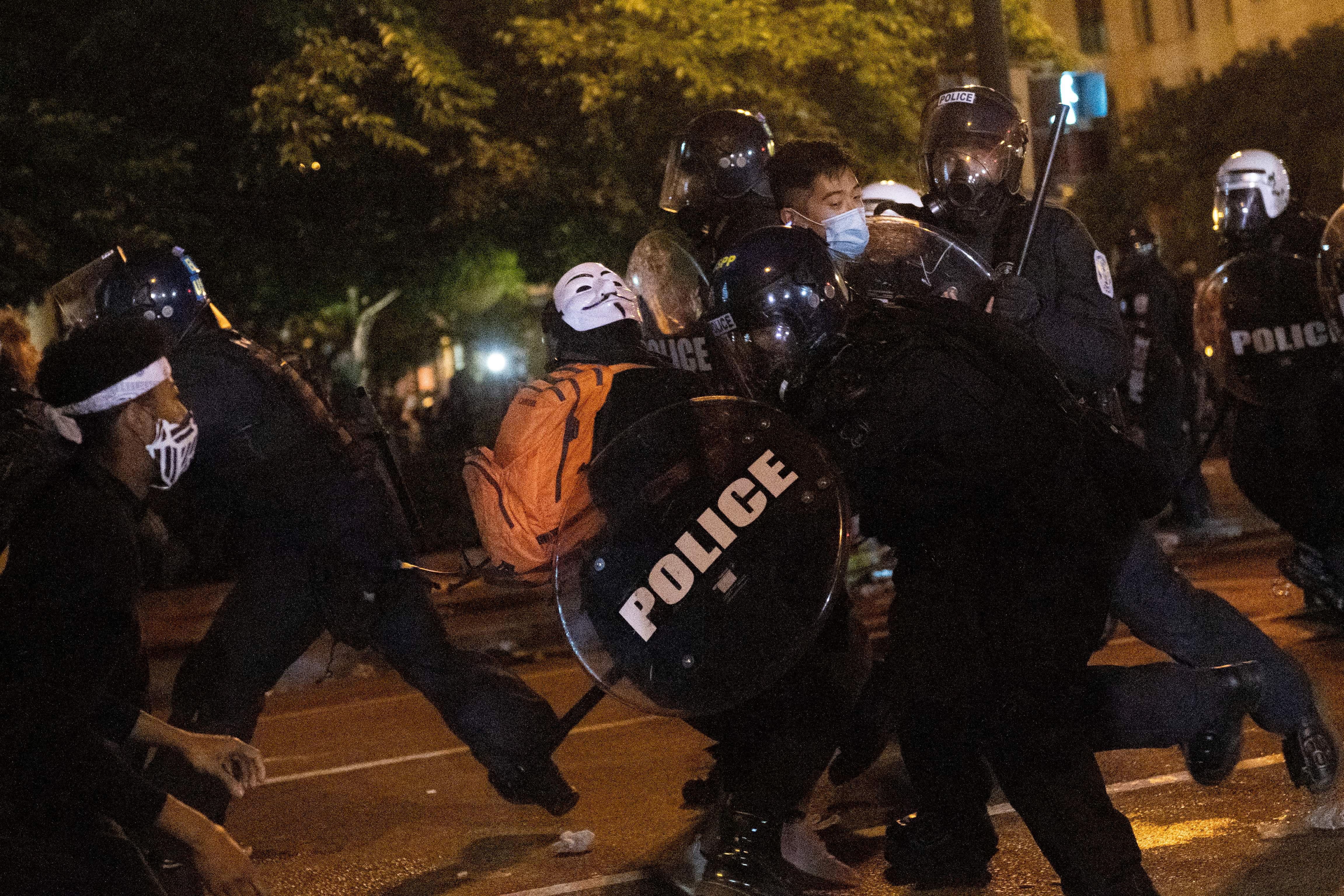 Police charge at protesters on a dark street.