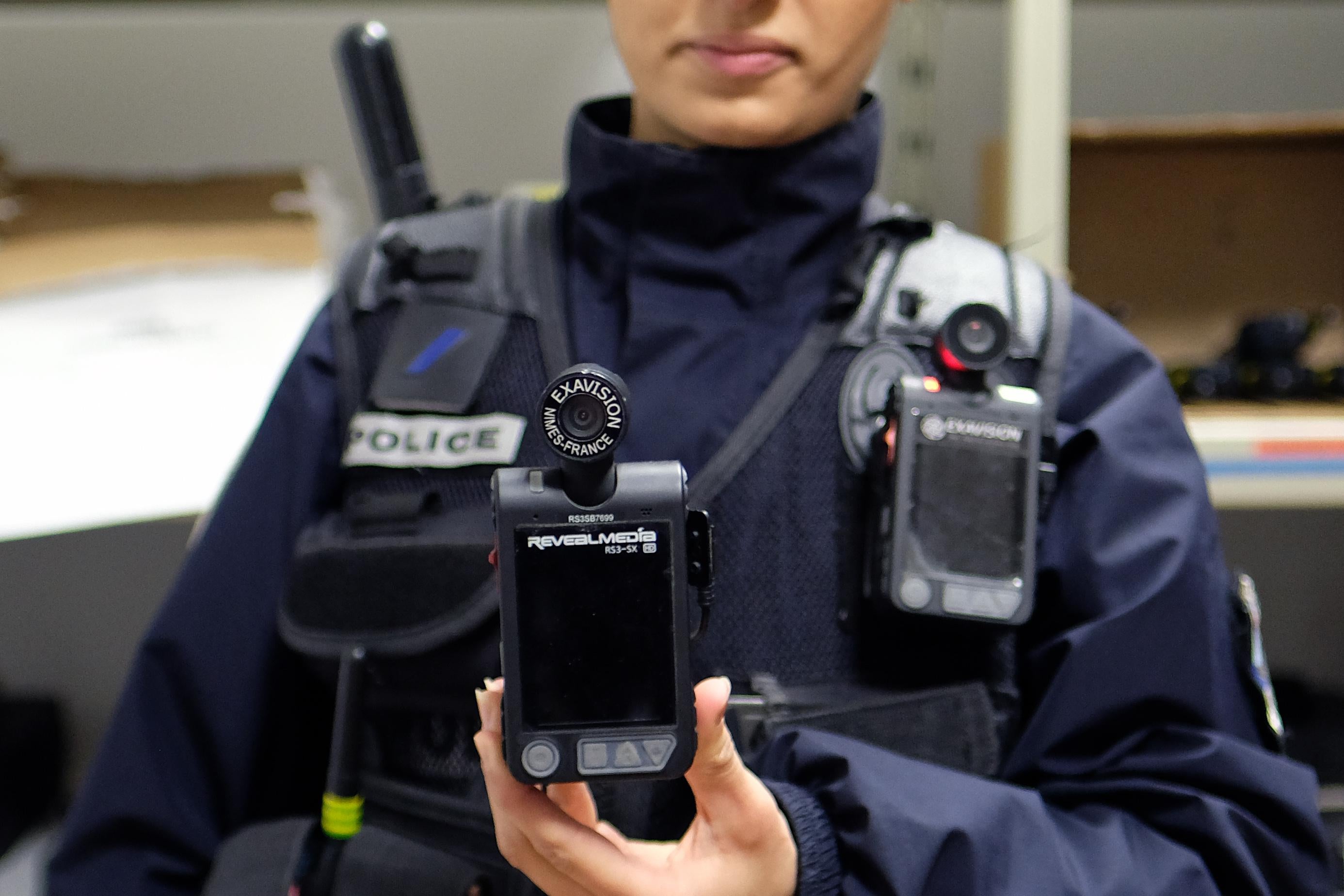 A person in police gear holds up a body camera.