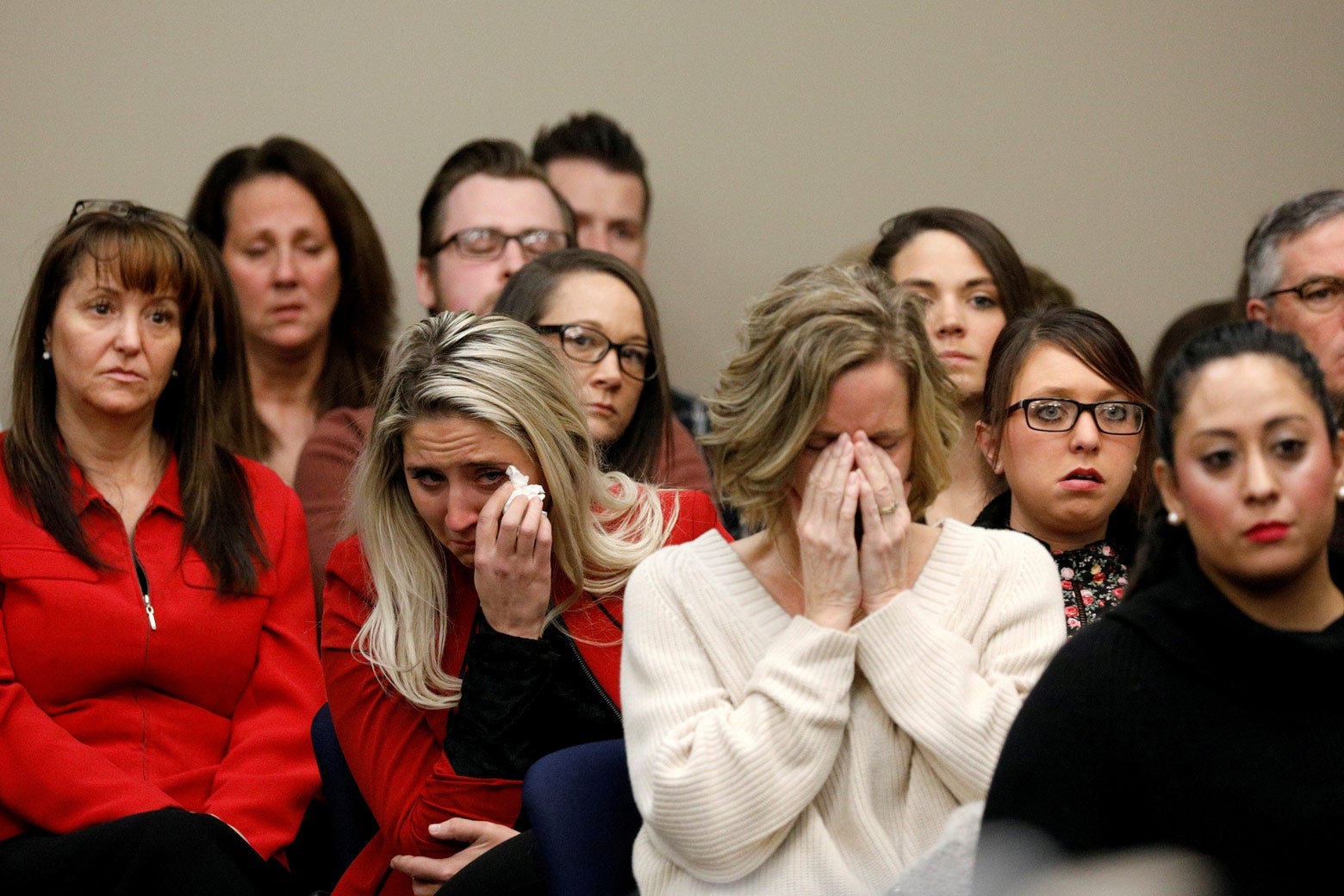 People seated in rows in court. Two women are crying.
