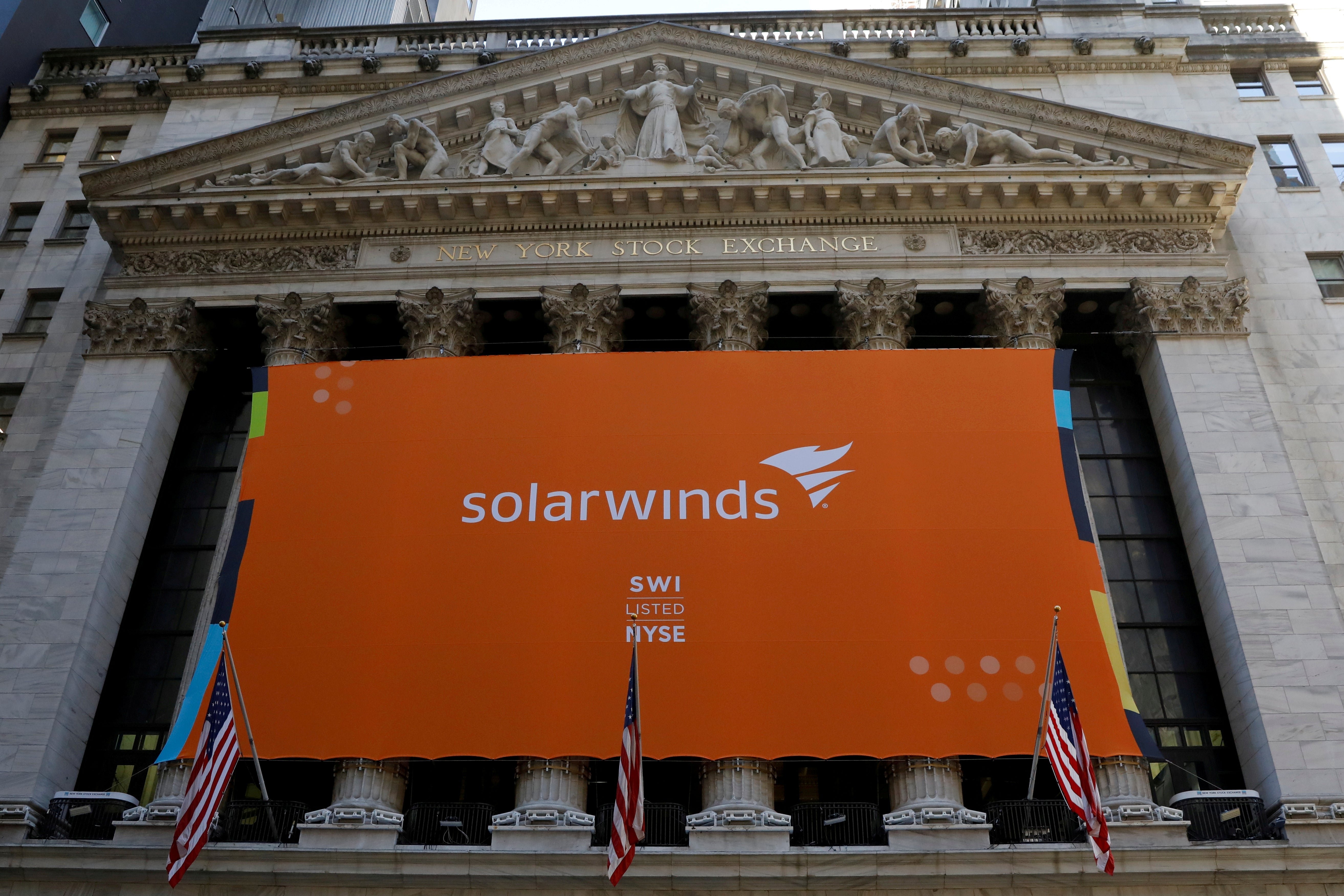 A large orange SolarWinds banner hanging on the front of the New York Stock Exchange building.