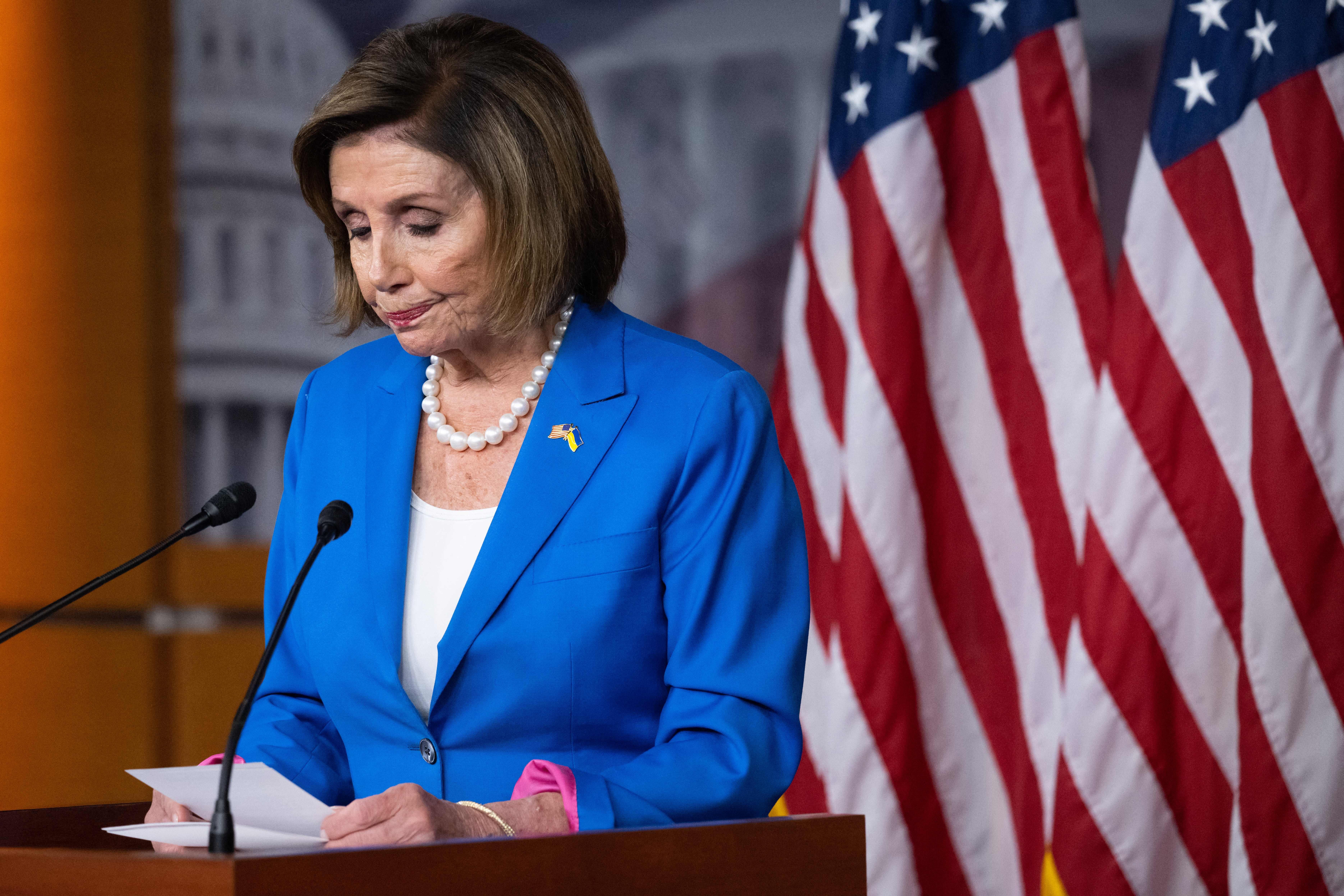 Pelosi looks down at her notes as she stands behind a podium.