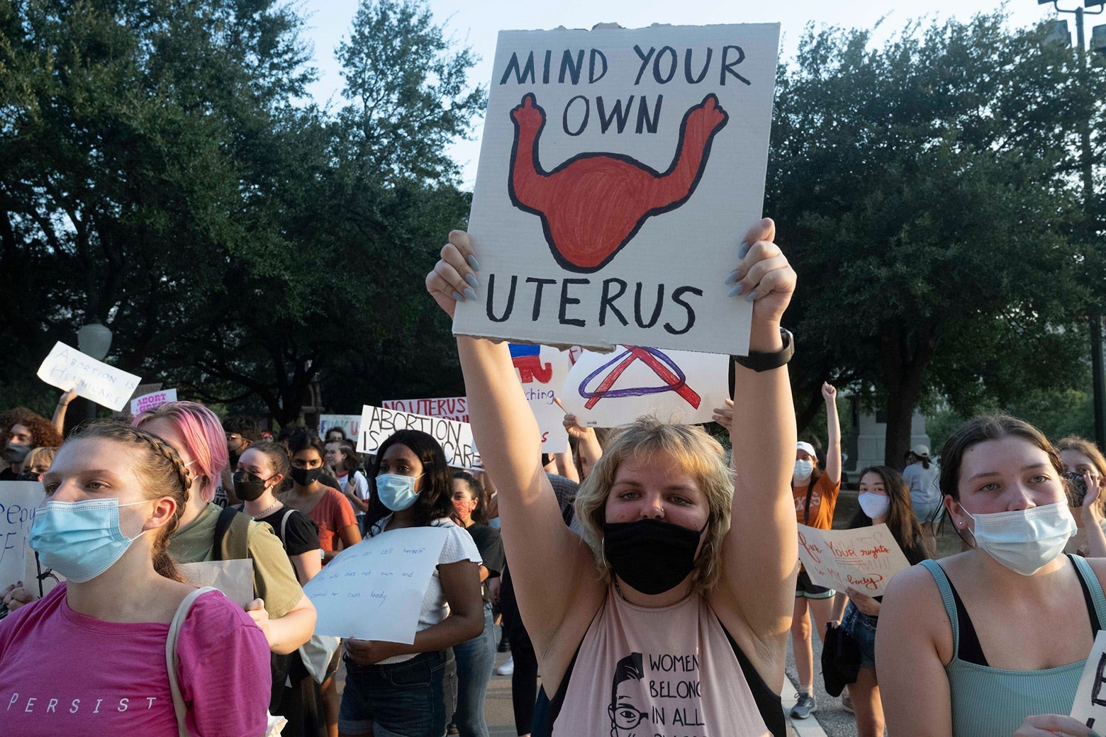 Women hold up signs, including one that says, "Mind your own uterus." 