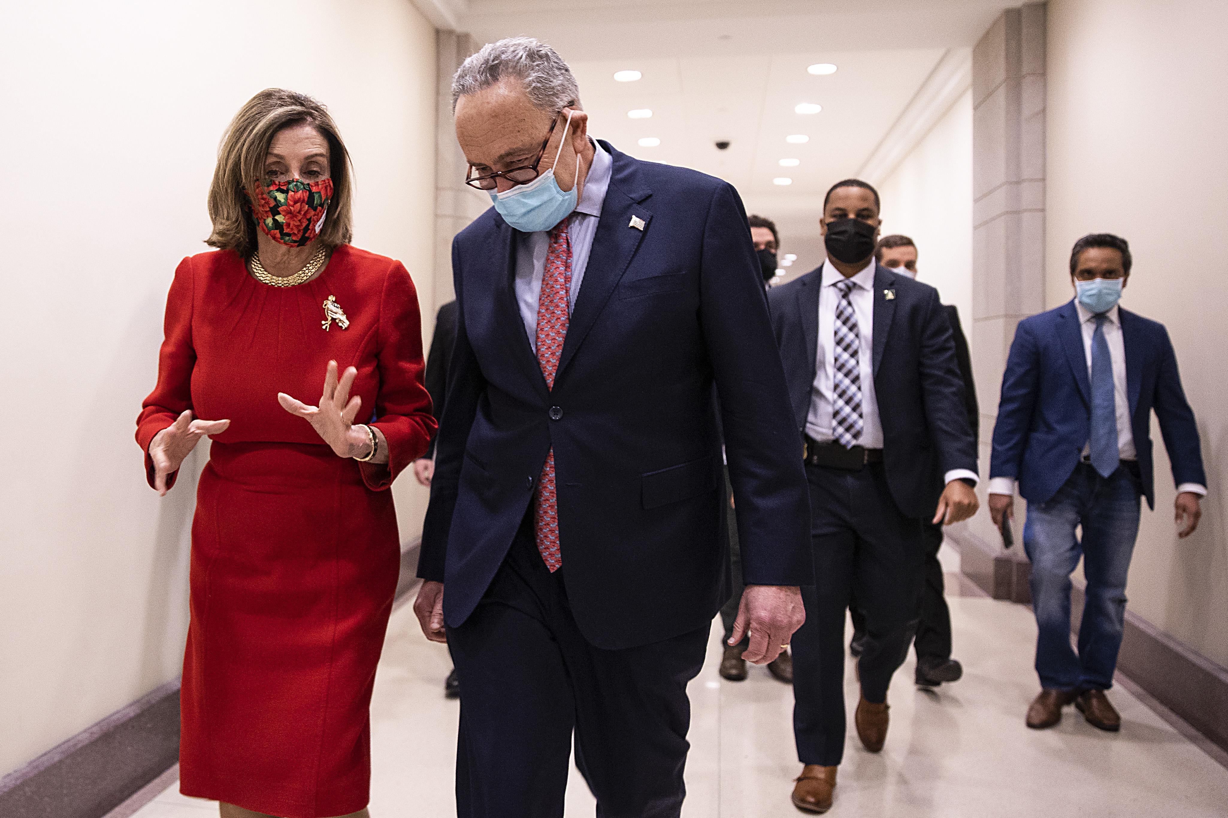 Nancy Pelosi talks to Chuck Schumer as they walk down a hallway together