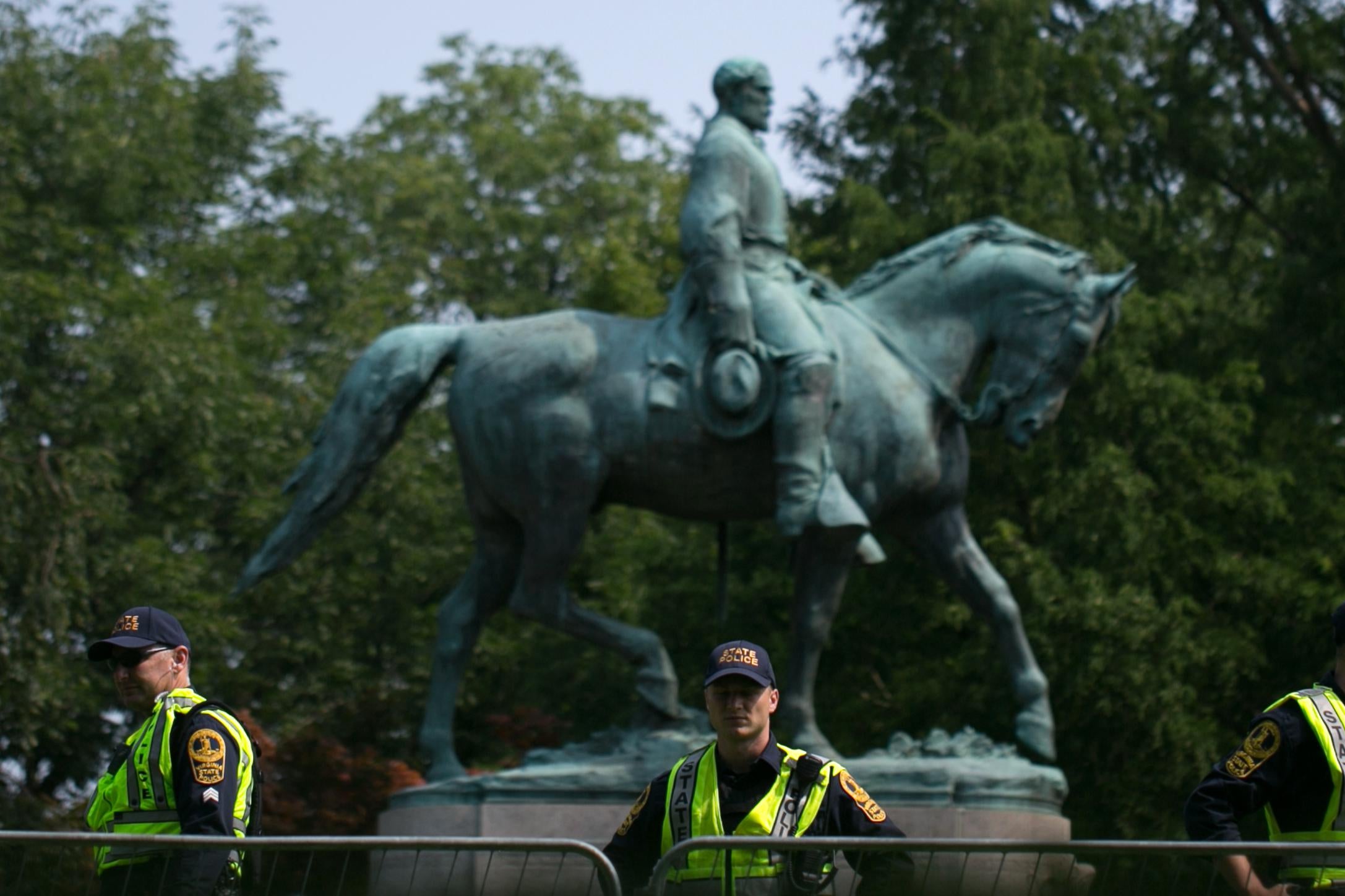 Three officers wearing neon safety vests stand in front of the Lee statue on a sunny day