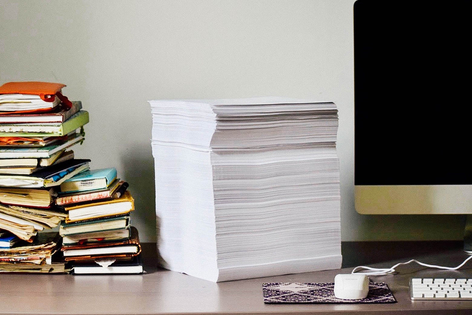 A stack of printed papers on a desk, flanked by a computer and books.