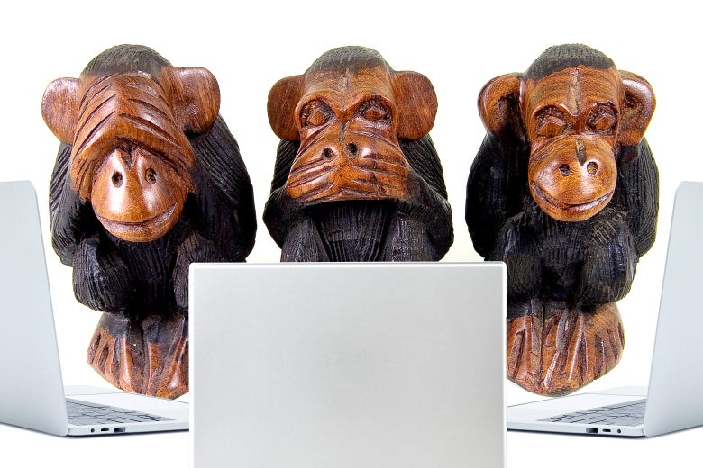 Three "see no evil, speak no evil, hear no evil" monkey statues sitting in front of laptops.