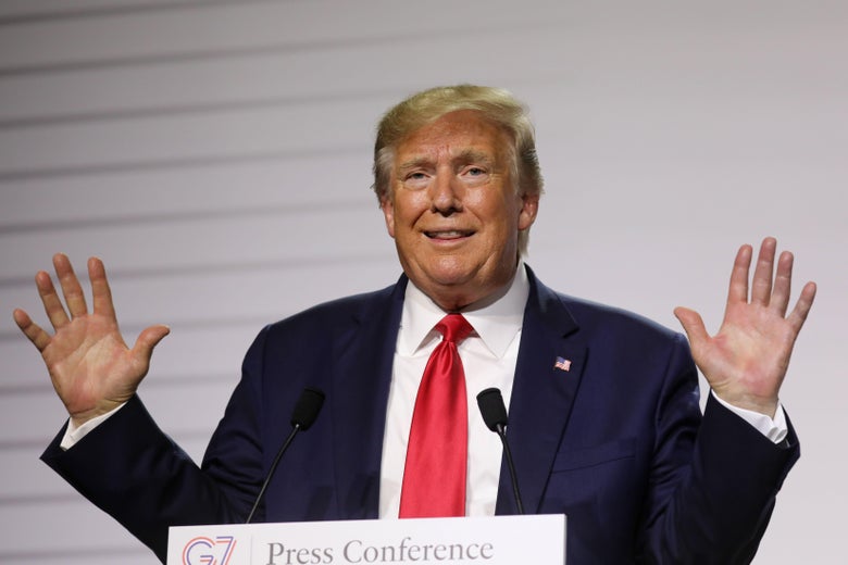 Donald Trump raises his hands while speaking into a mic at a lectern.