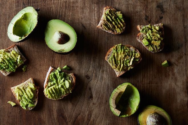 Two halved avocados next to slices of avocado-covered bread. The left avocado is green, the right brown.