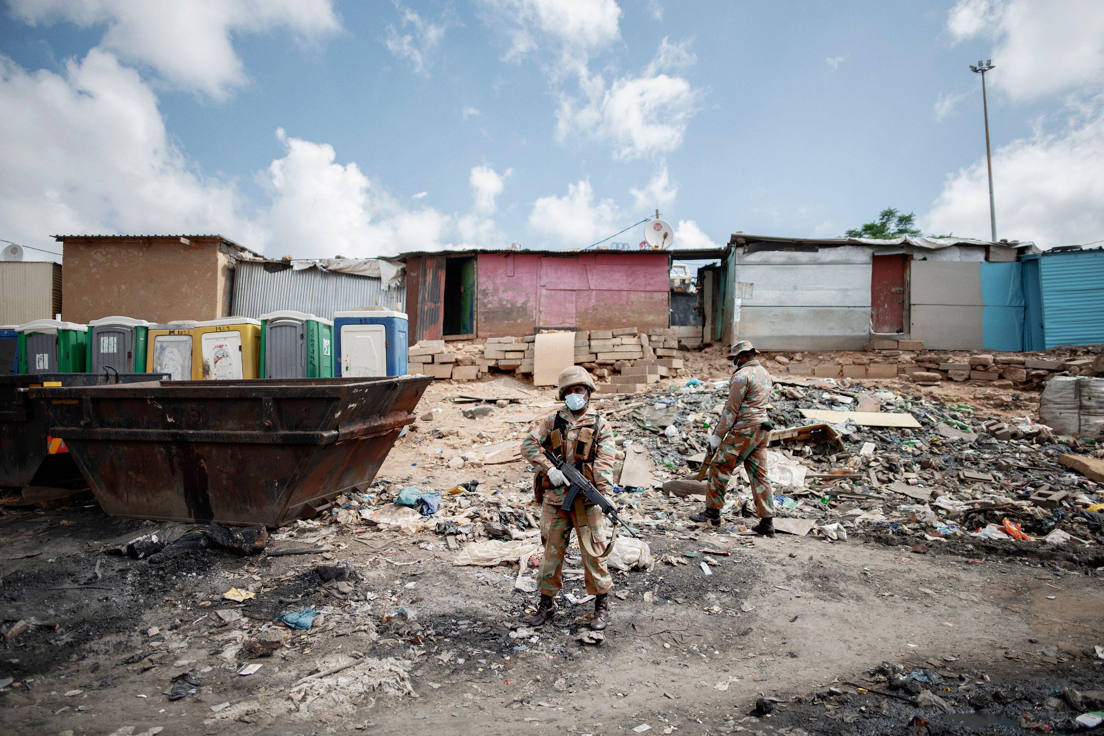 Mask-wearing troops carry guns in front of shanty houses in a South African township.