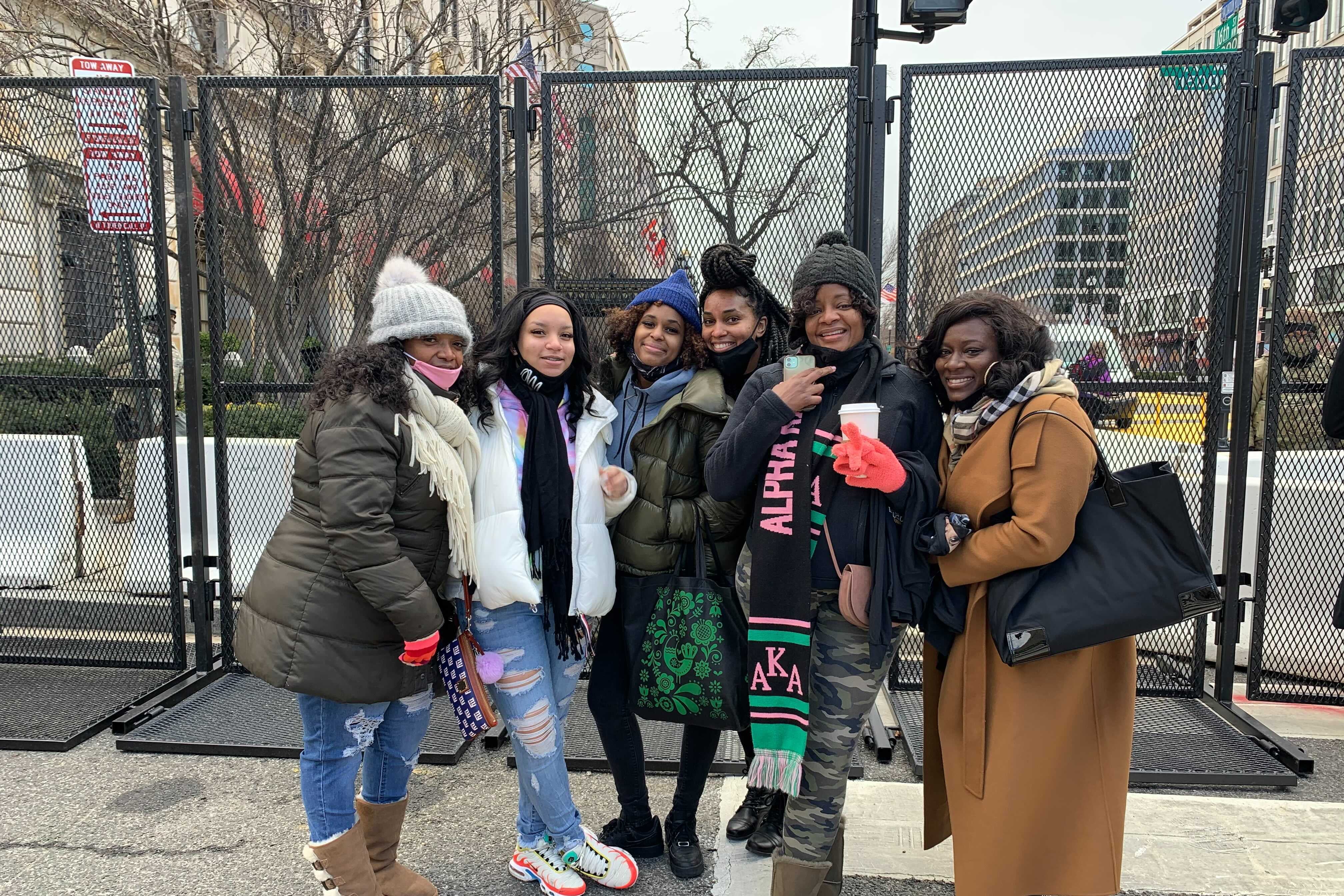 Six women stand smiling in front of a fence