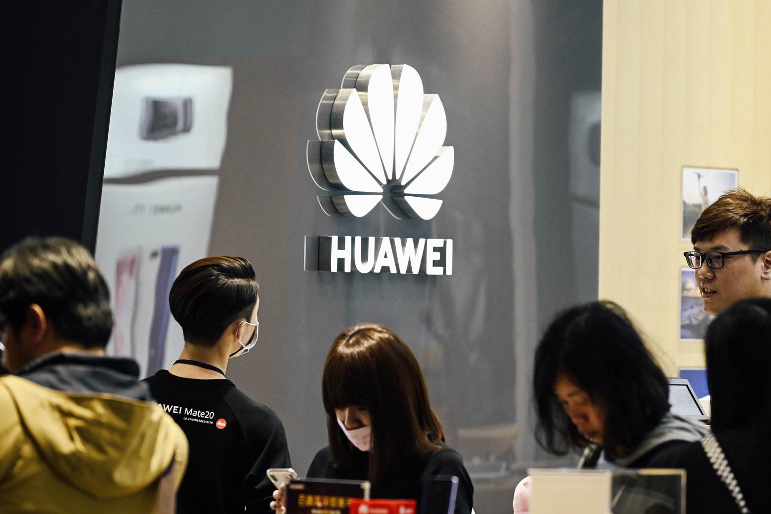 People stand next to a Huawei logo at a mall.