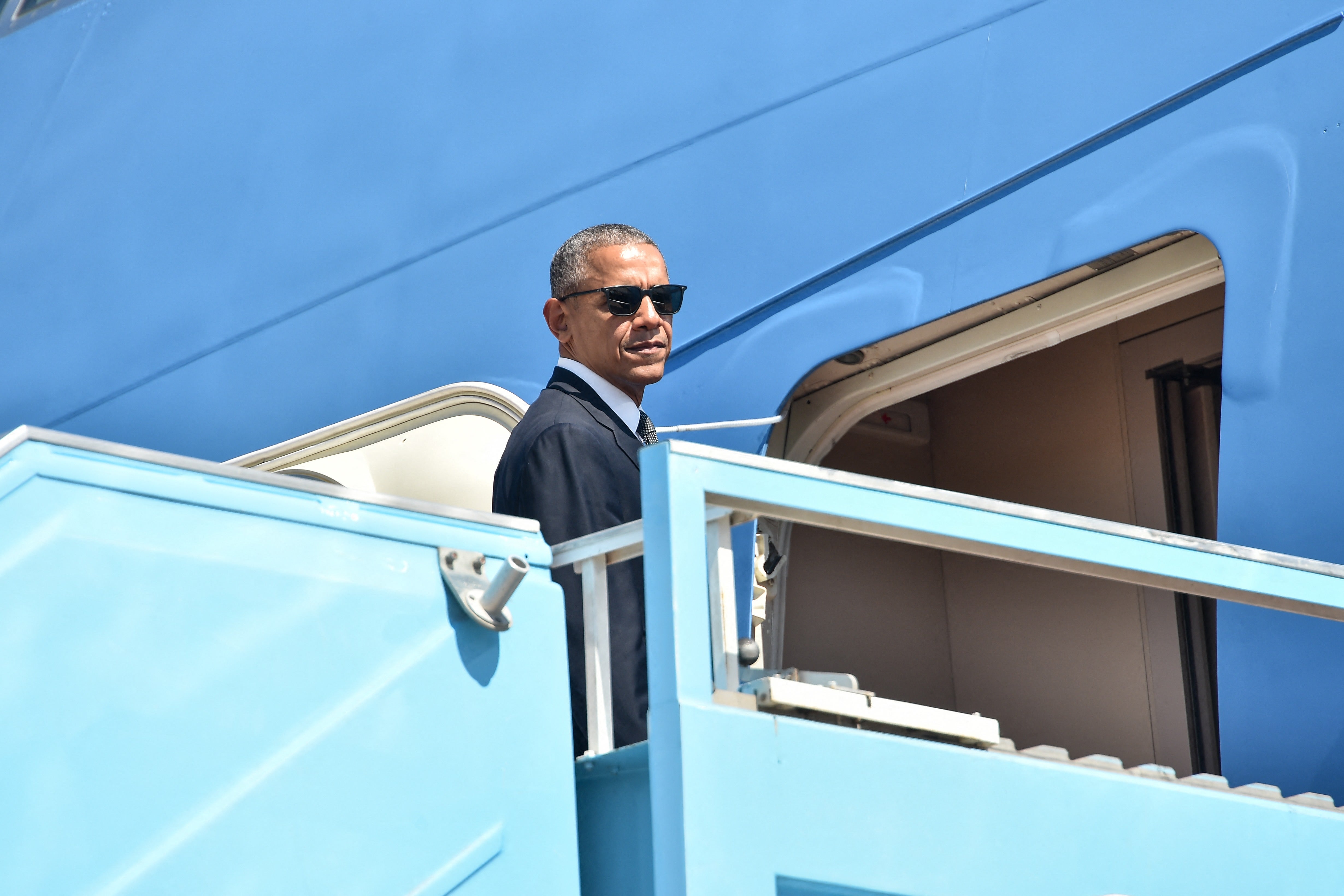 Barack Obama wears sunglasses and steps onto a plane.