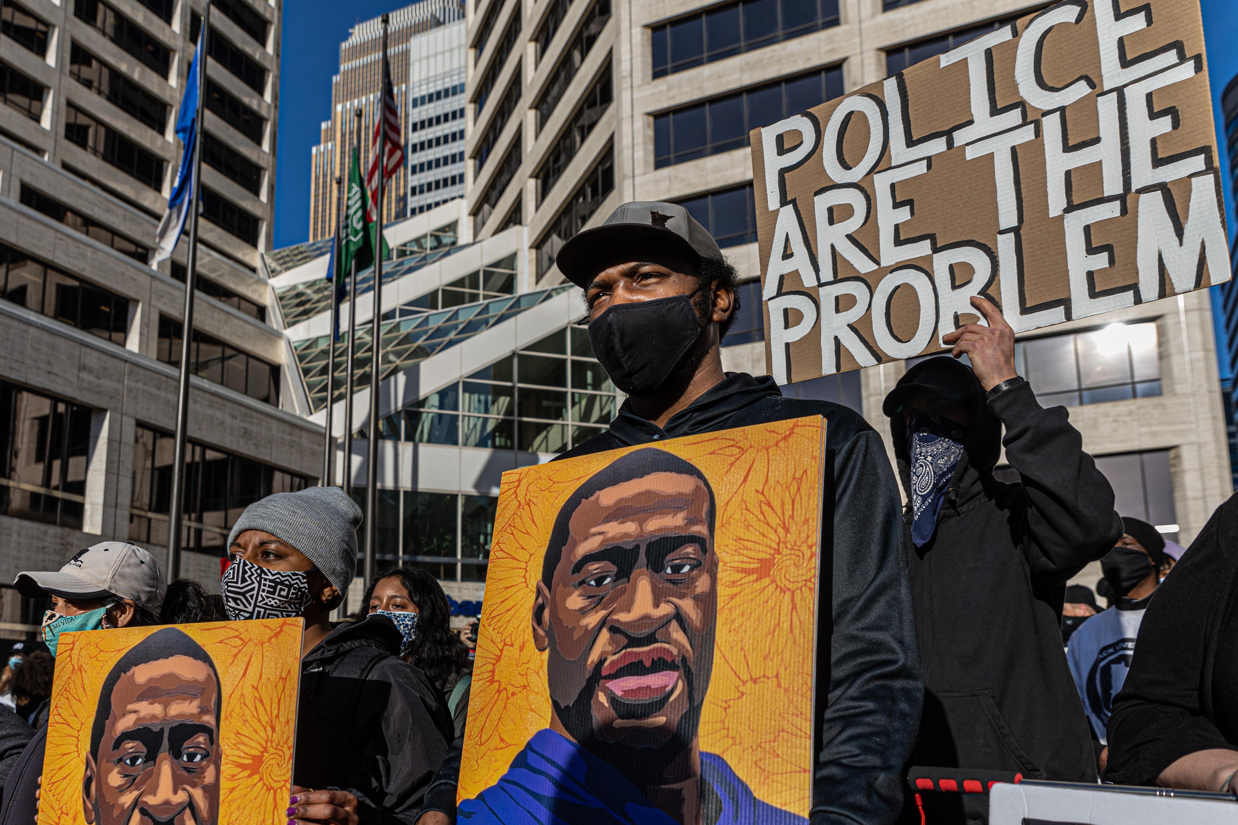 Protesters in masks hold up paintings of George Floyd and signs that say things like, "Police are the problem."