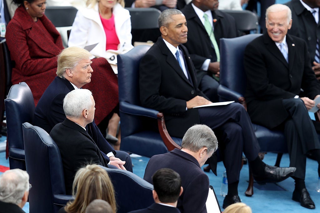 Biden, smiling, looks past Barack Obama toward Donald Trump as they are seated on a dais surrounded by other dignitaries.