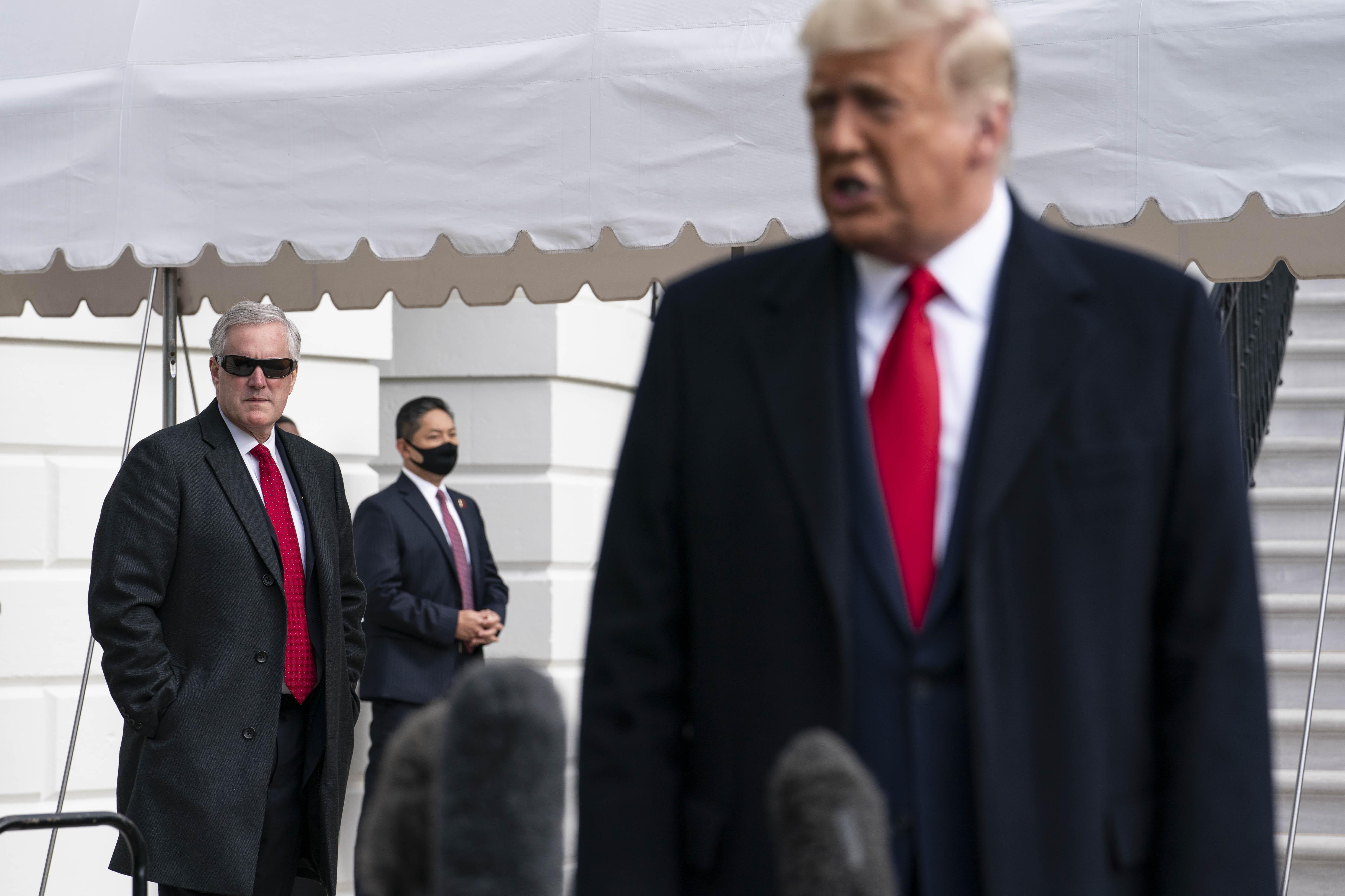 Meadows wearing sunglasses behind Trump emulating almost his entire look, with a oversized black coat and red tie.