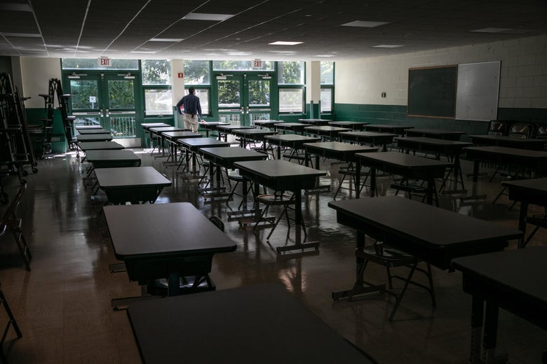 A dark, empty school cafeteria with tables spaced out for social distancing