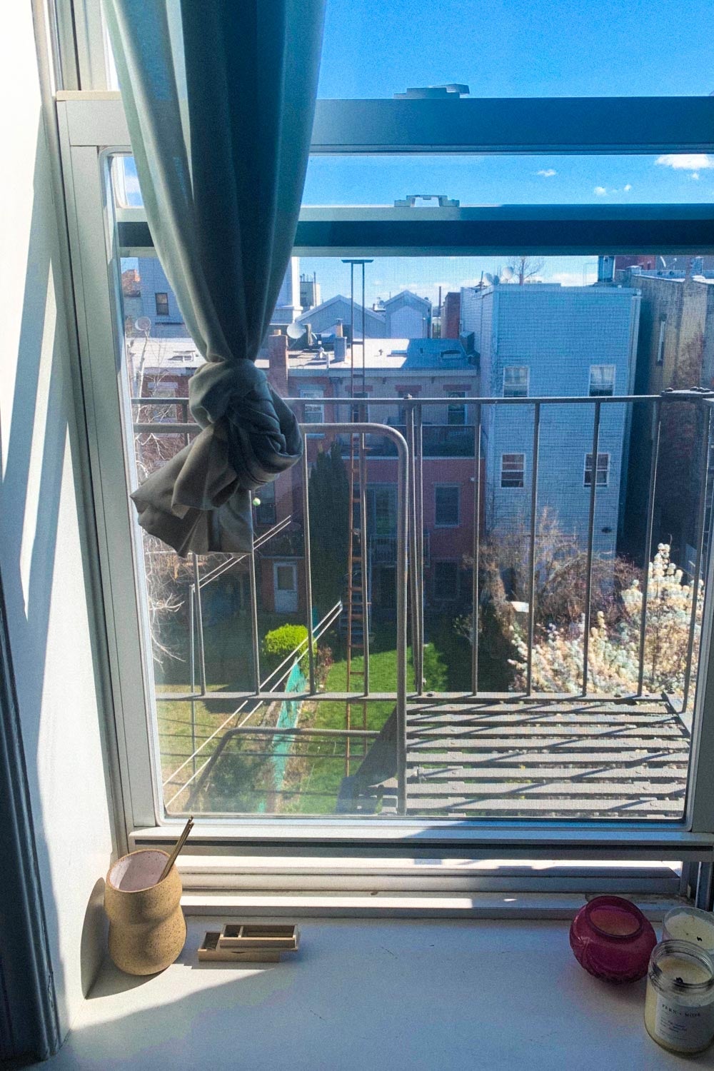 A window onto a fire escape facing a grass courtyard on a sunny early spring day.