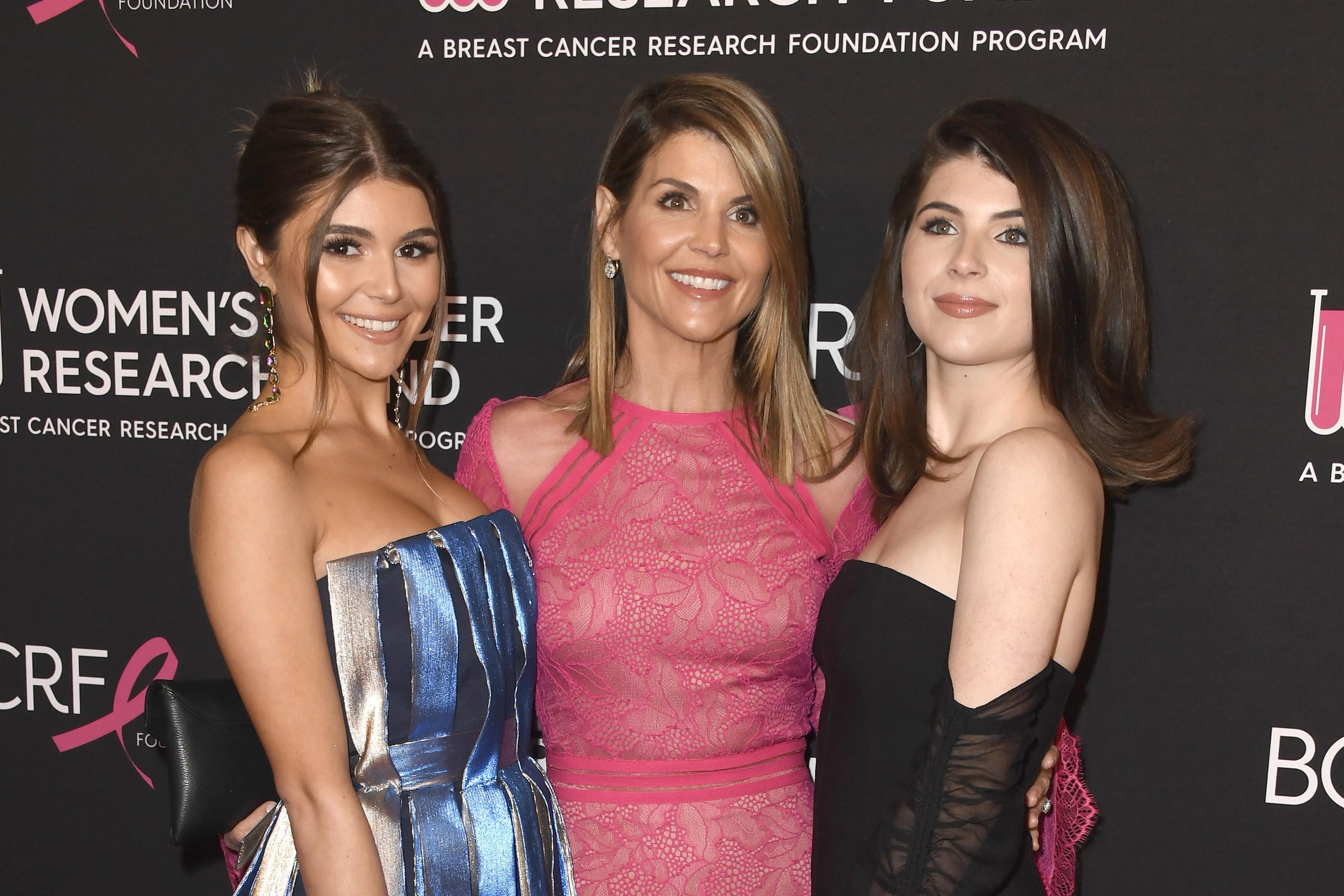 Olivia Jade Giannulli, Lori Loughlin, and Isabella Rose Giannulli standing together in formalwear in front of a step-and-repeat for the gala they're attending behind them.