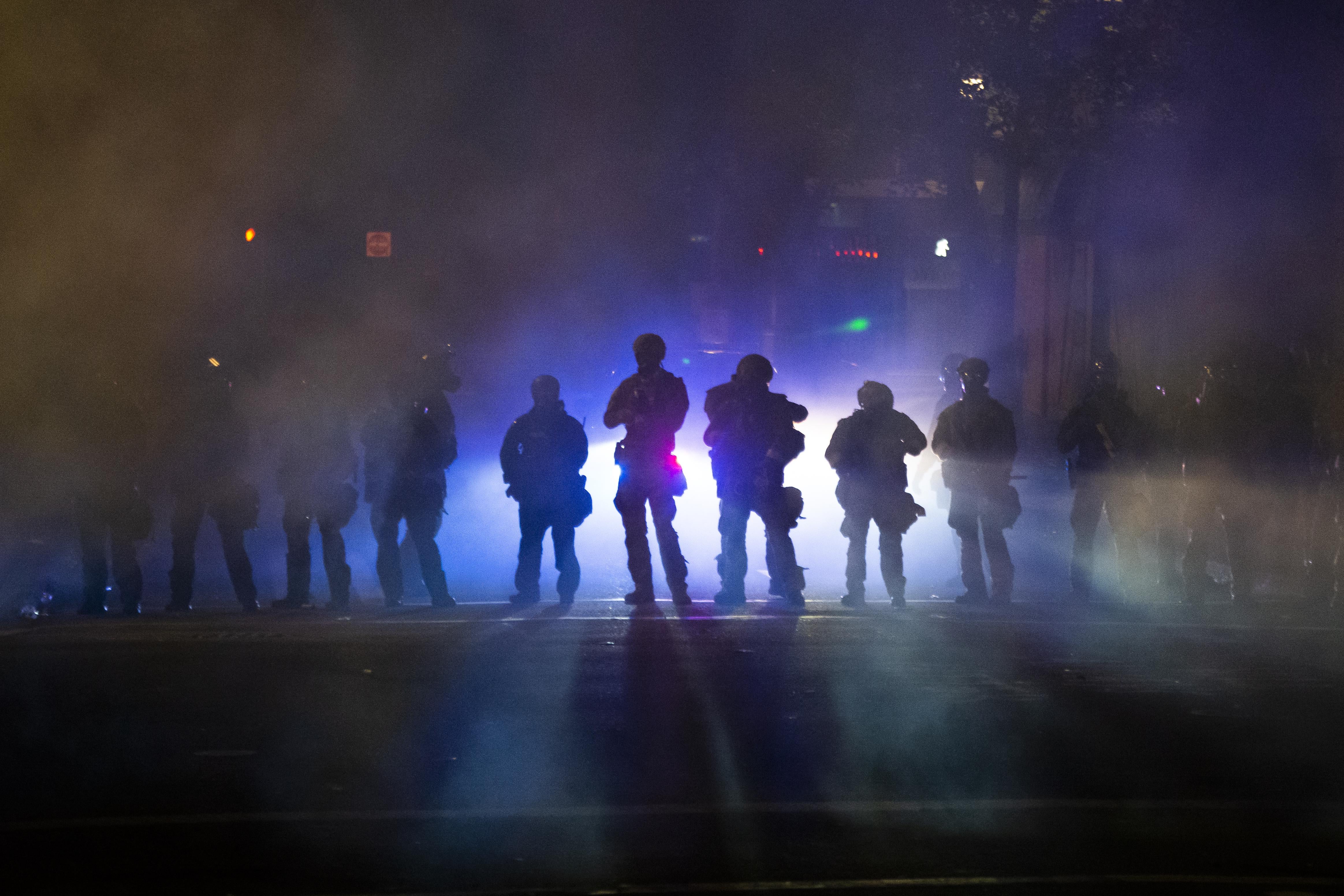 Heavily armed officers seen through smoke and tear gas. 