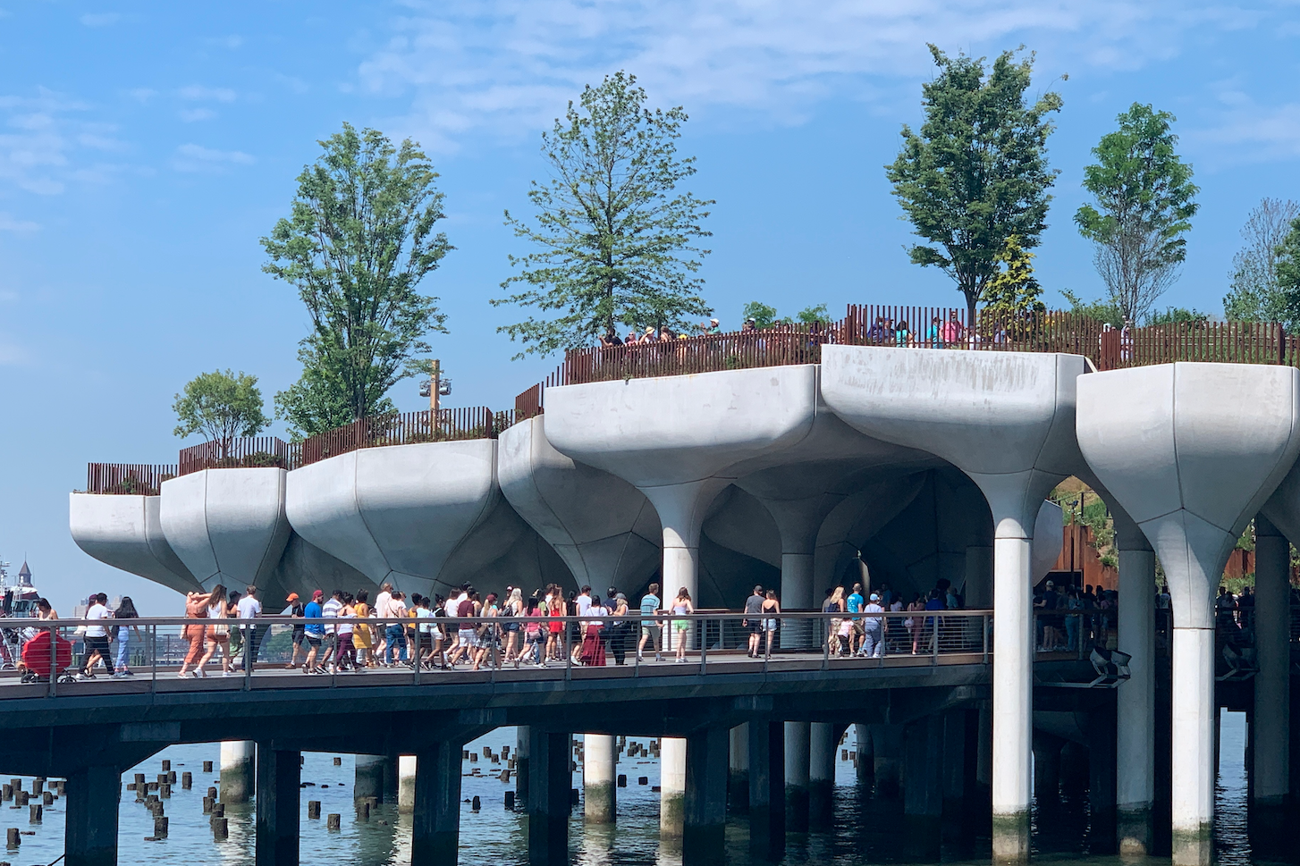 Visitors walk along a gangway to Little Island, which is made up of concrete potlike structures suspended above the Hudson River and grouped together to form a park